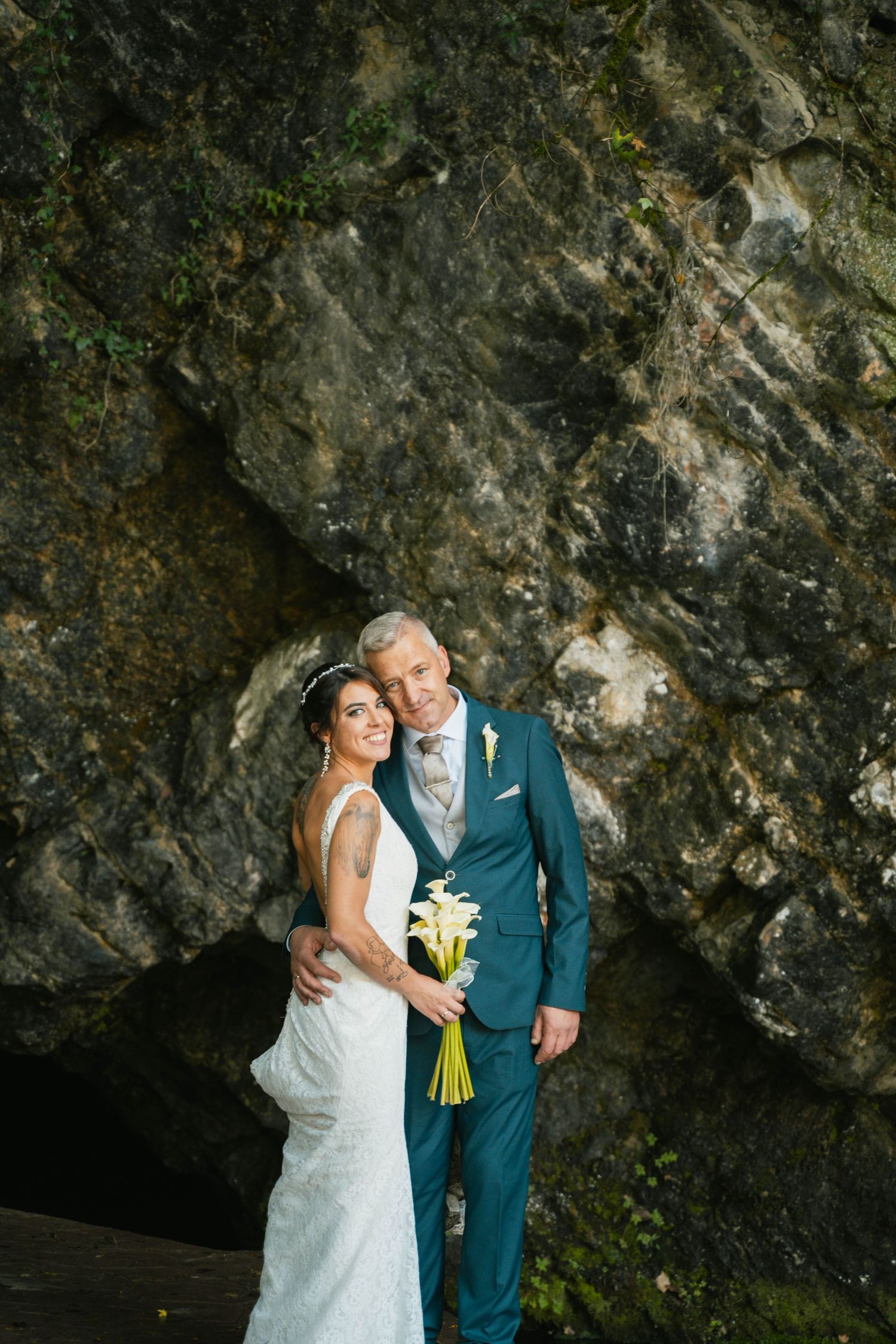 A couple poses against a dramatic rock formation backdrop in formal wedding attire.