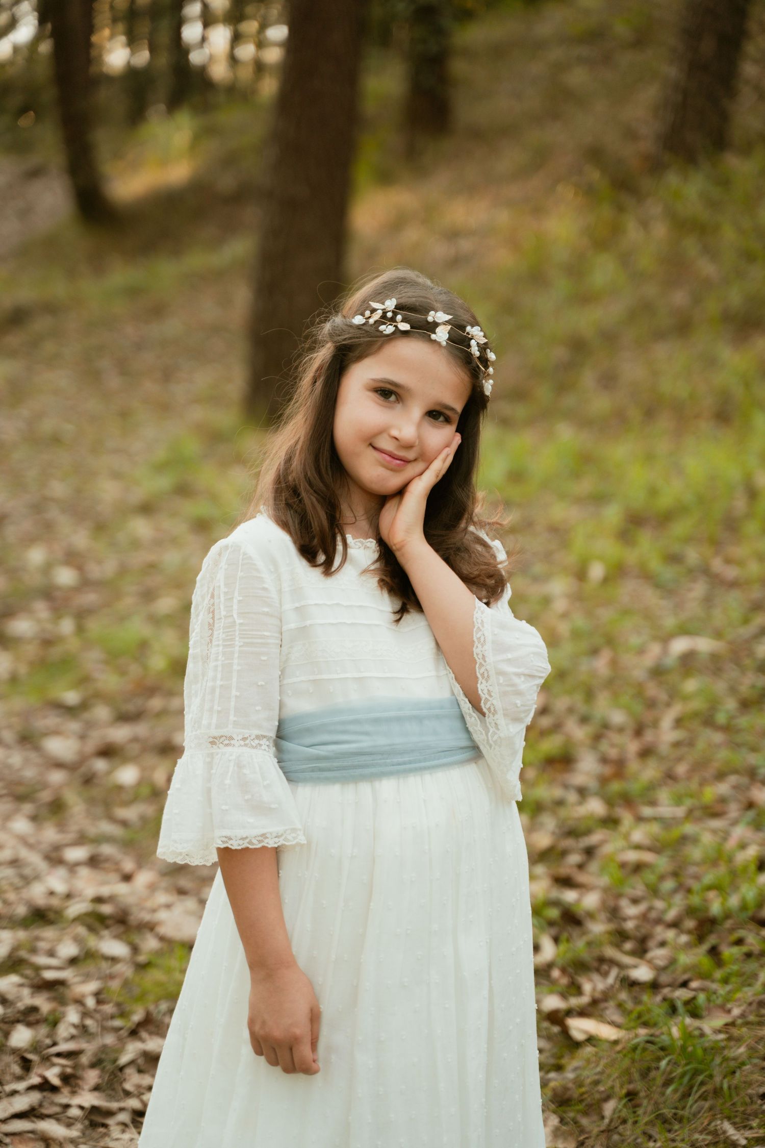 Ethereal woodland portrait featuring a white dress with blue sash and delicate floral crown.