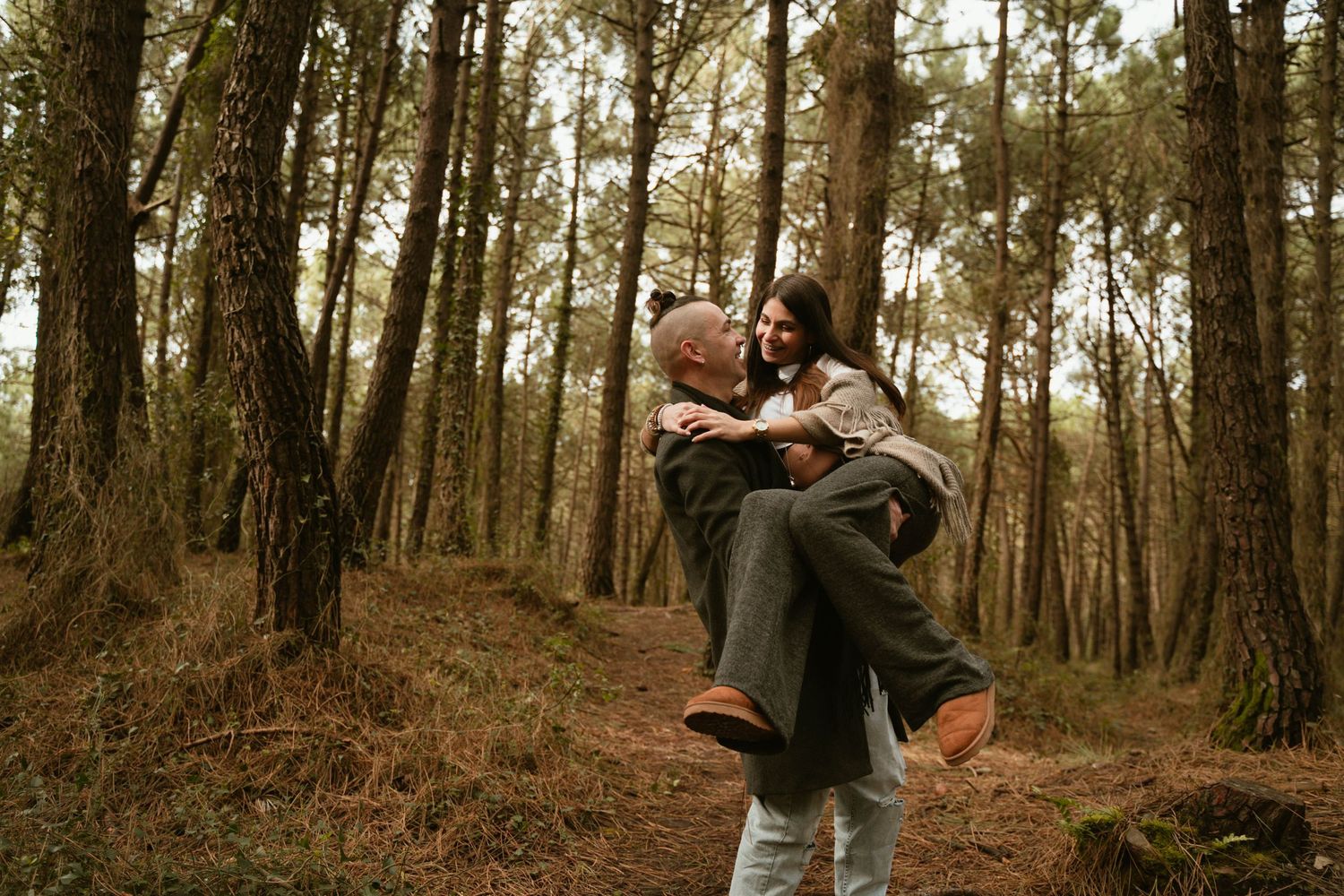 Playful maternity photo of a couple having fun in a wooded forest setting.