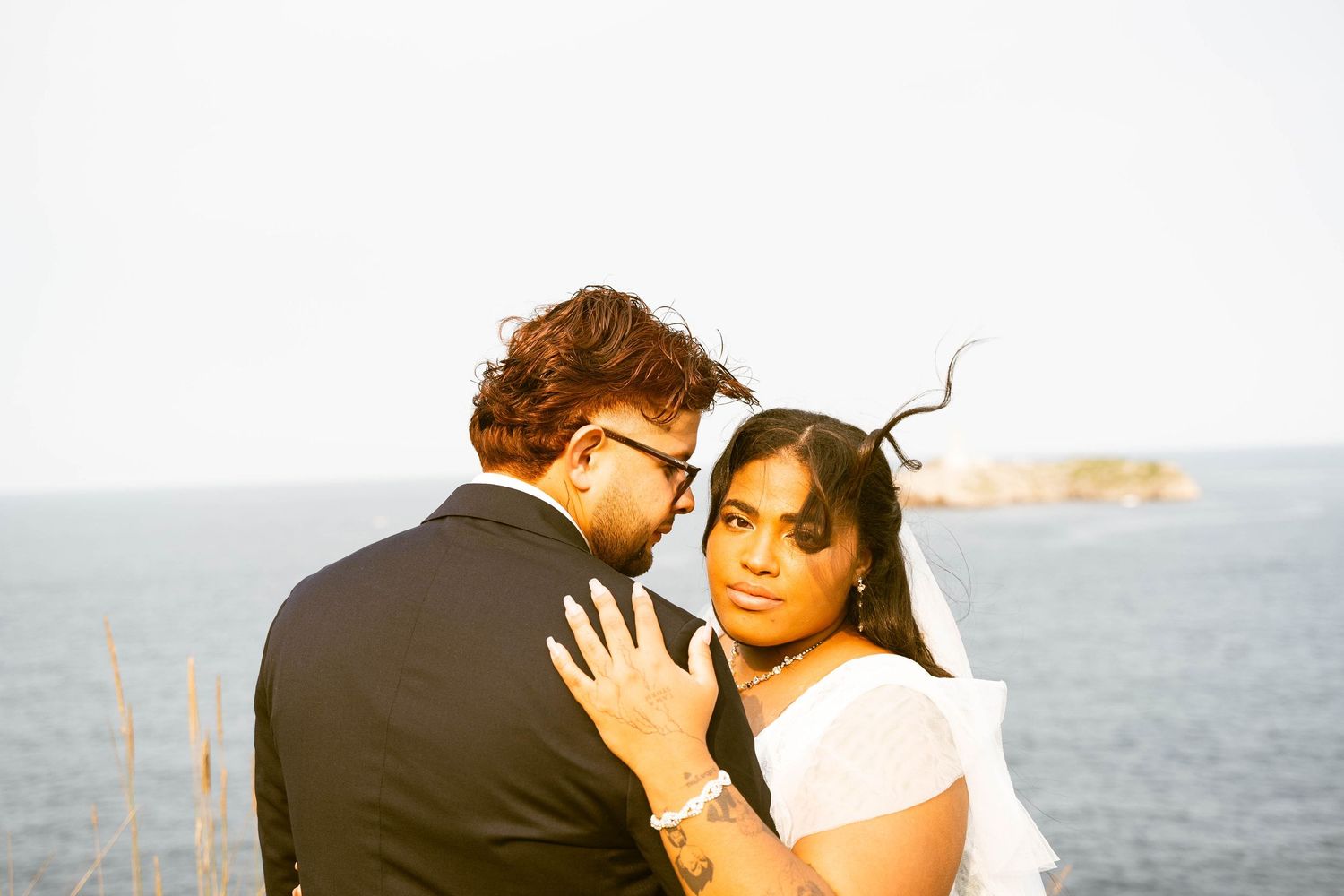 A wedding couple embraces against an ocean backdrop during golden hour.