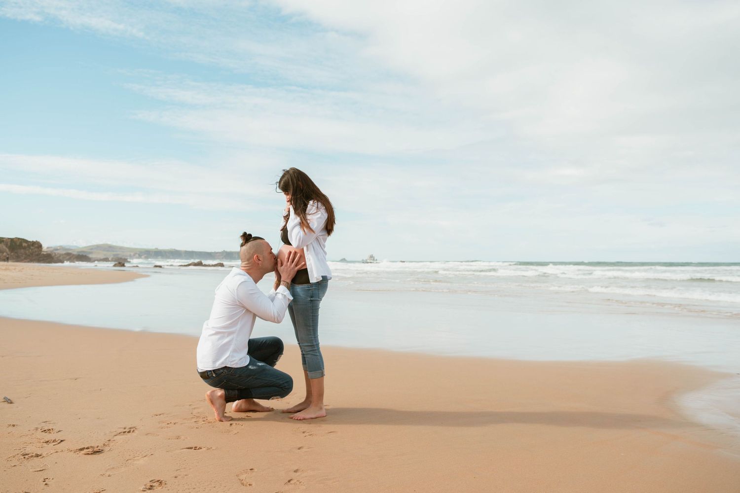 A romantic beach proposal moment captured on a sandy shoreline with blue ocean waves in the background.