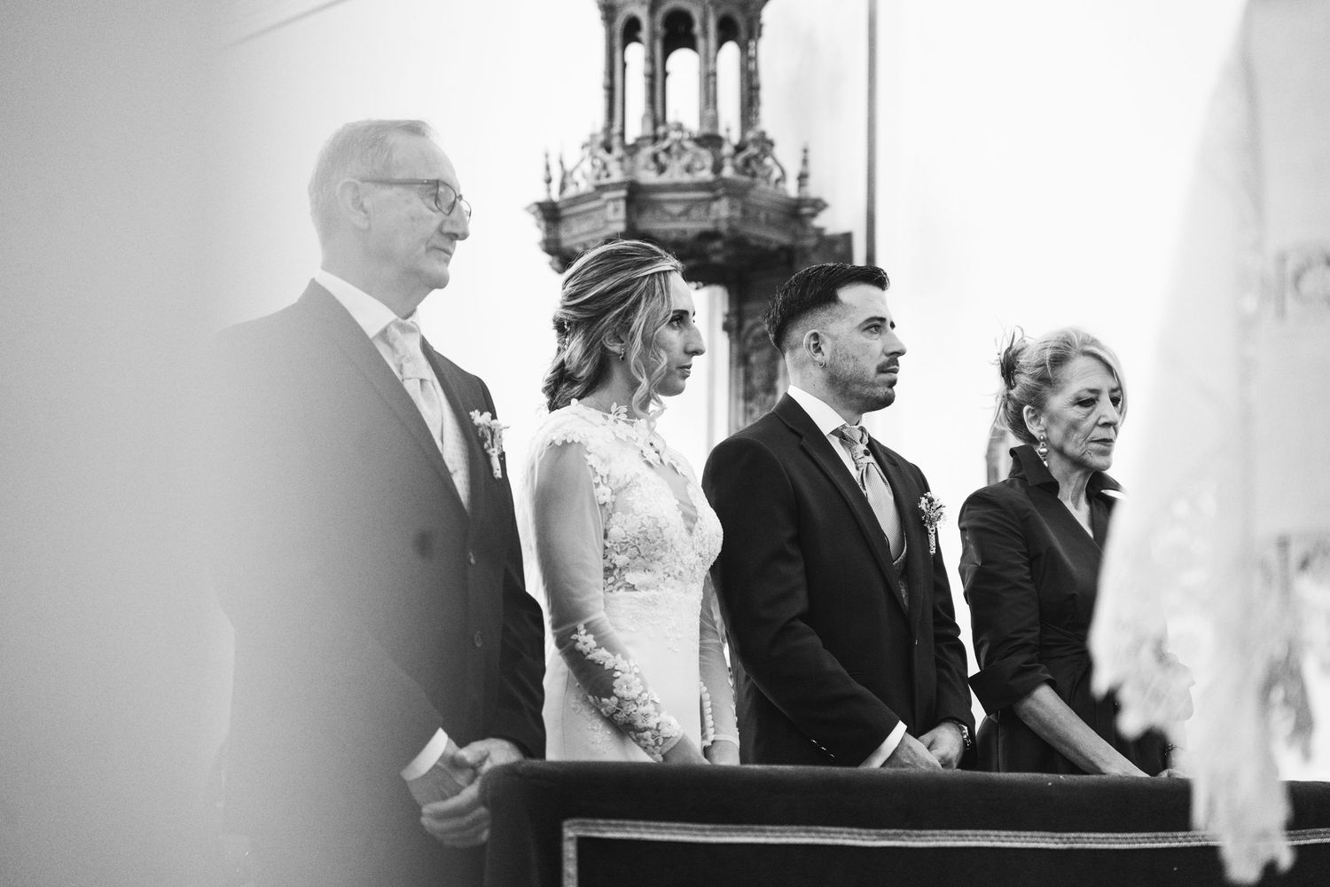 Wedding ceremony participants stand solemnly in a church during the service.
