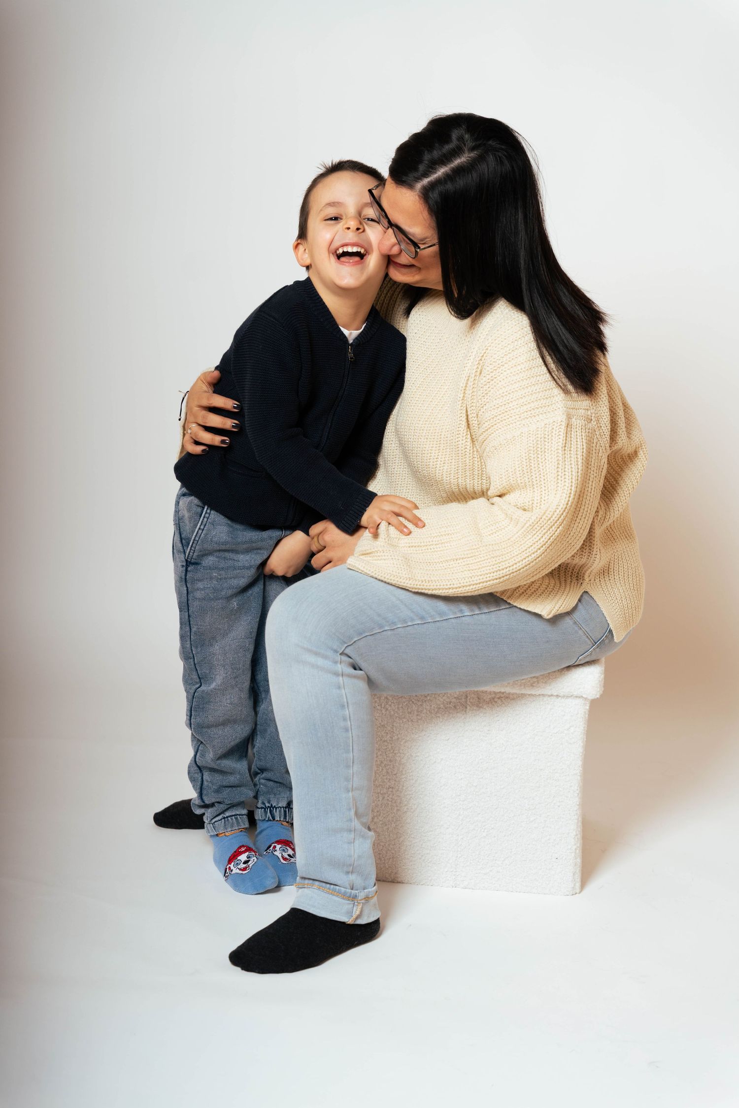 A series of playful studio portraits showing joyful interaction between a child in dark clothing and adult in beige sweater.