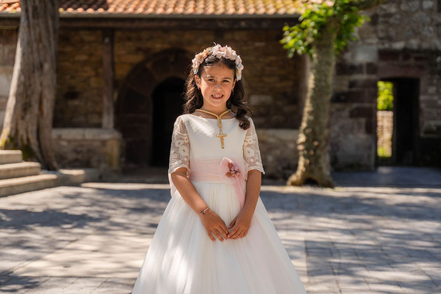Children in formal white outfits stand in front of historic stone building with terracotta roof.