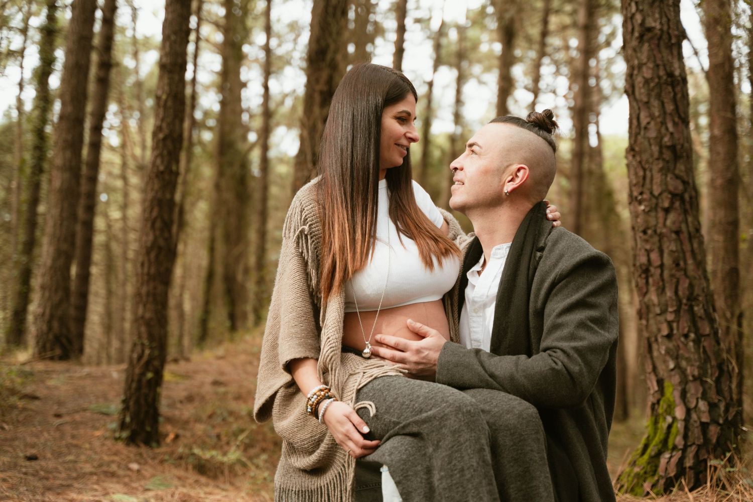 Couple sharing a loving moment during their maternity photoshoot in a pine forest.