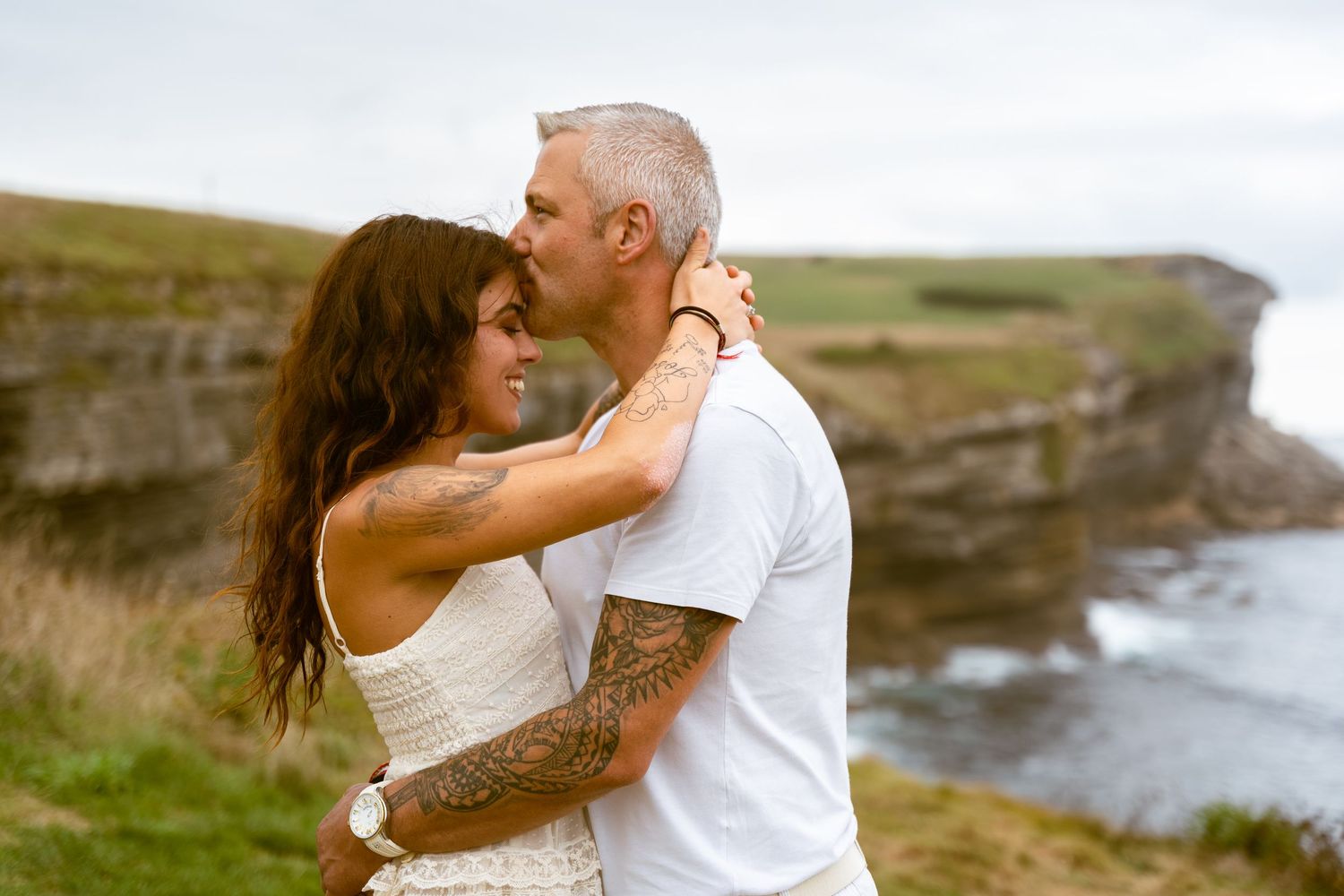 Couple embracing on dramatic coastal cliffs overlooking ocean.