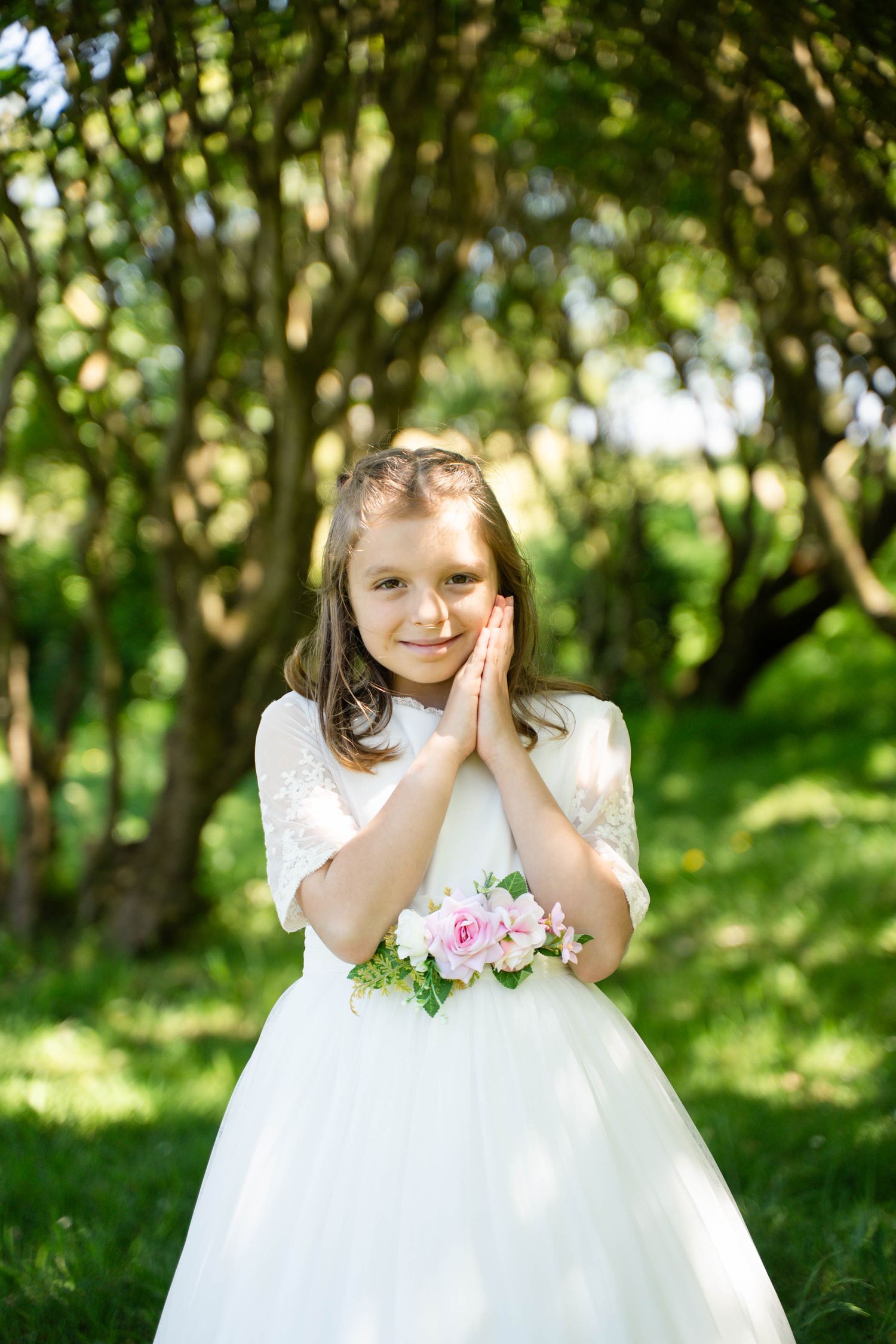 White dress with pink roses captured in a bright garden setting with dappled sunlight.