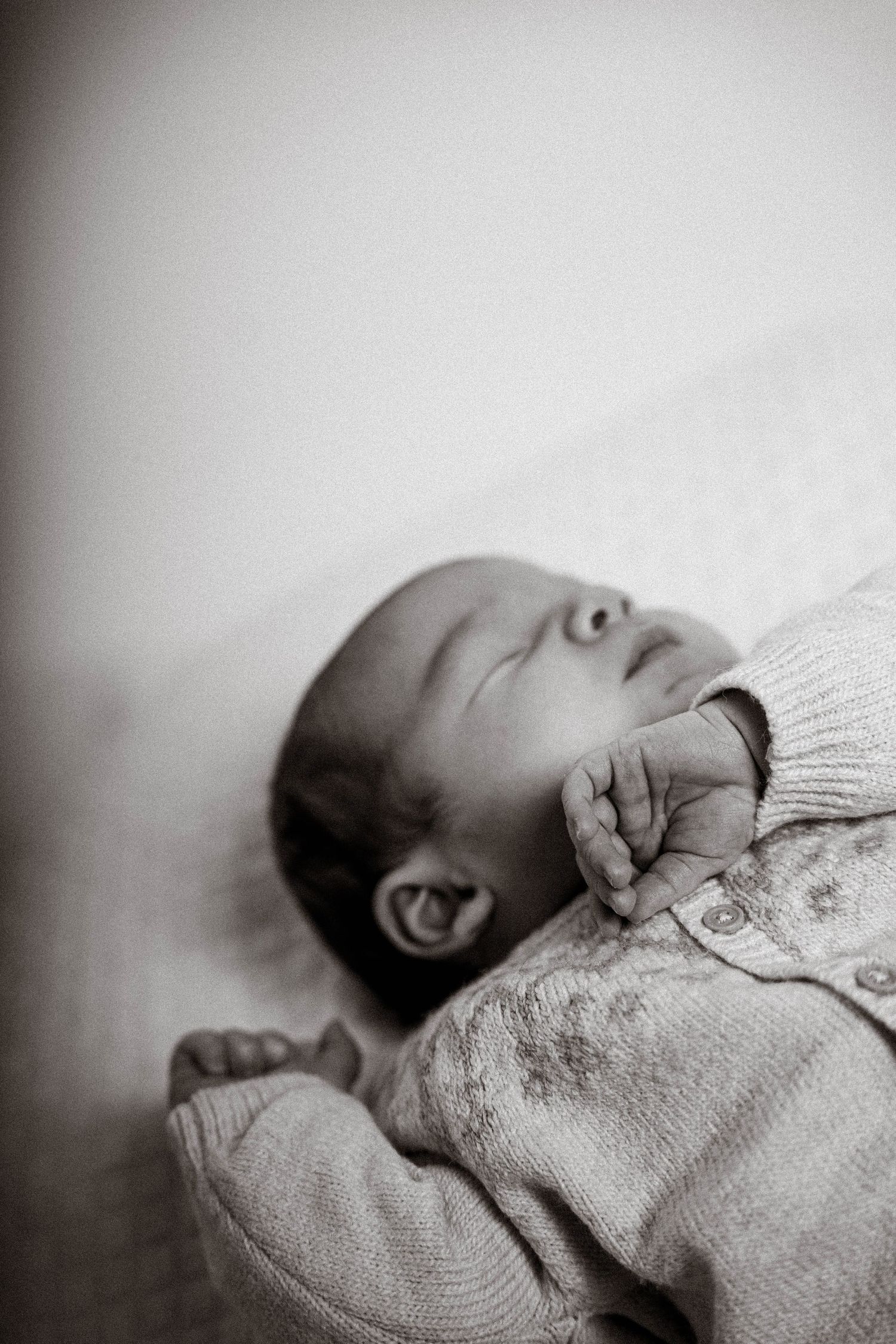 A black and white portrait of a sleeping baby wearing a light sweater lying on their back.
