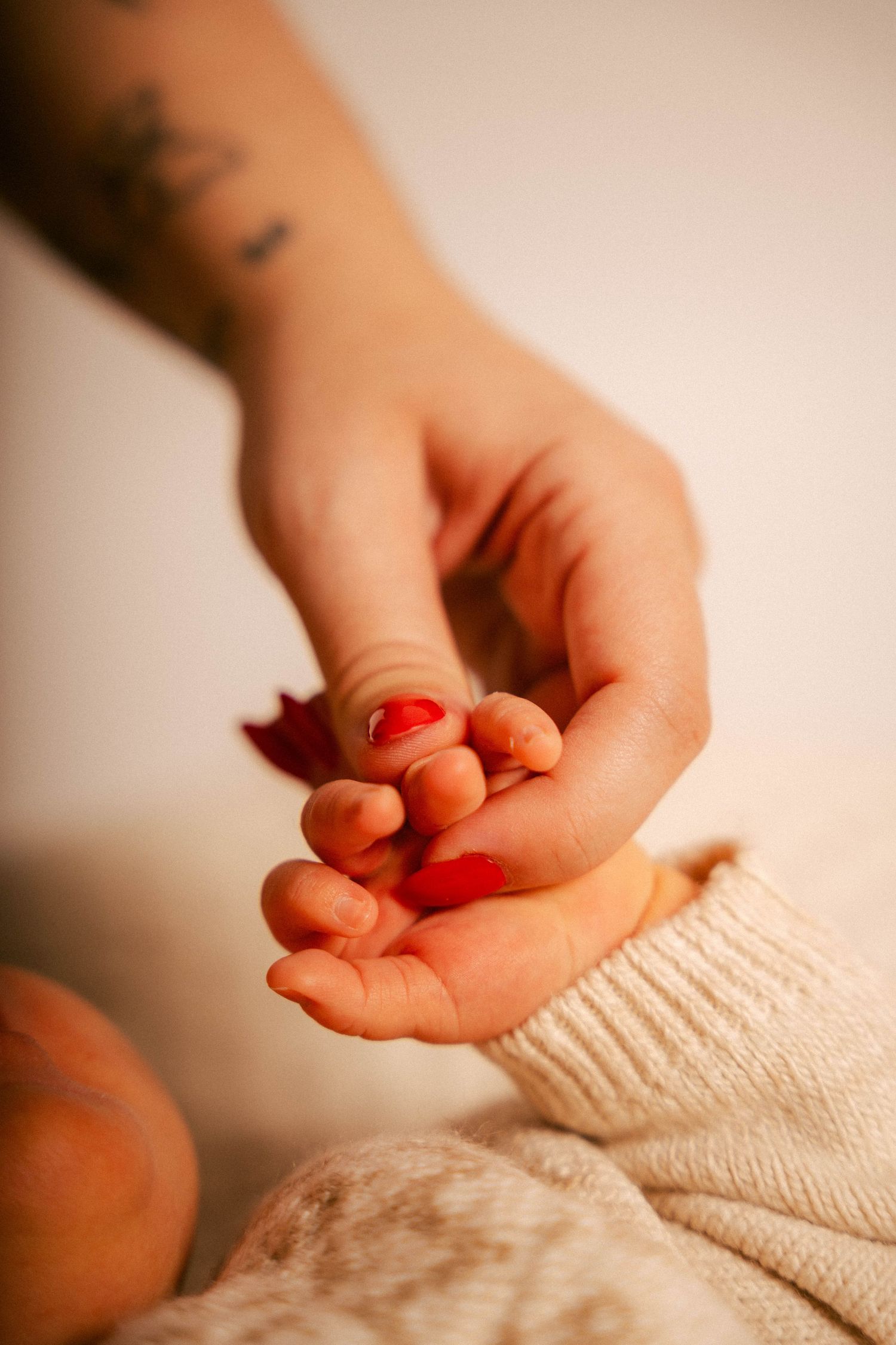 A close-up of hands touching tenderly, with red nail polish visible against a cream-colored sweater sleeve.