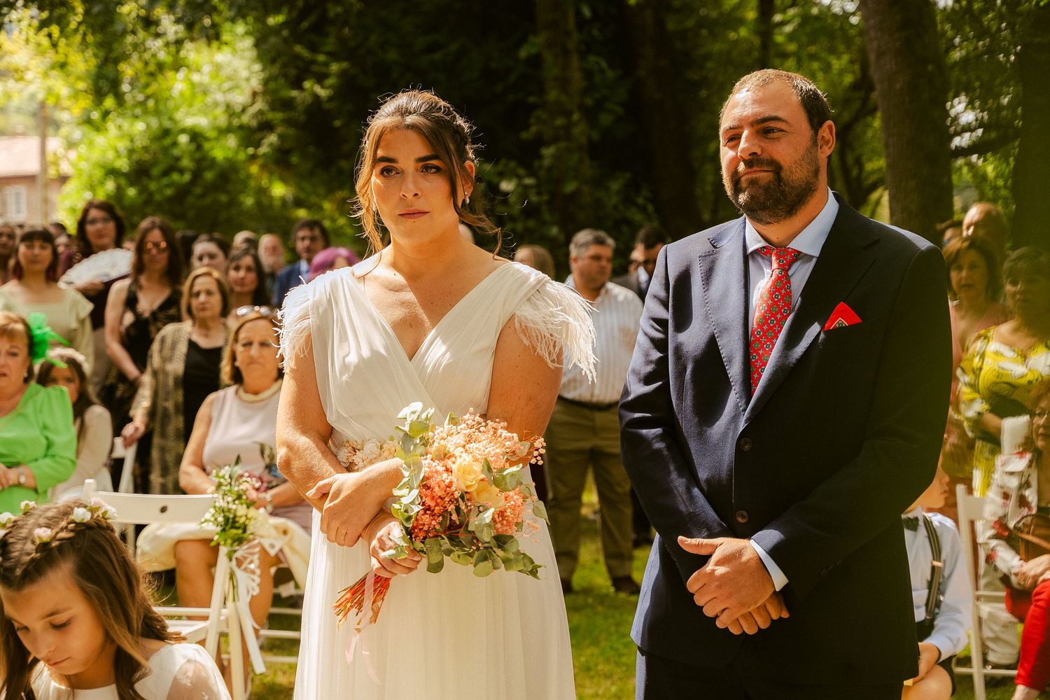 A couple exchanges vows during an outdoor garden wedding ceremony with guests watching in the background.