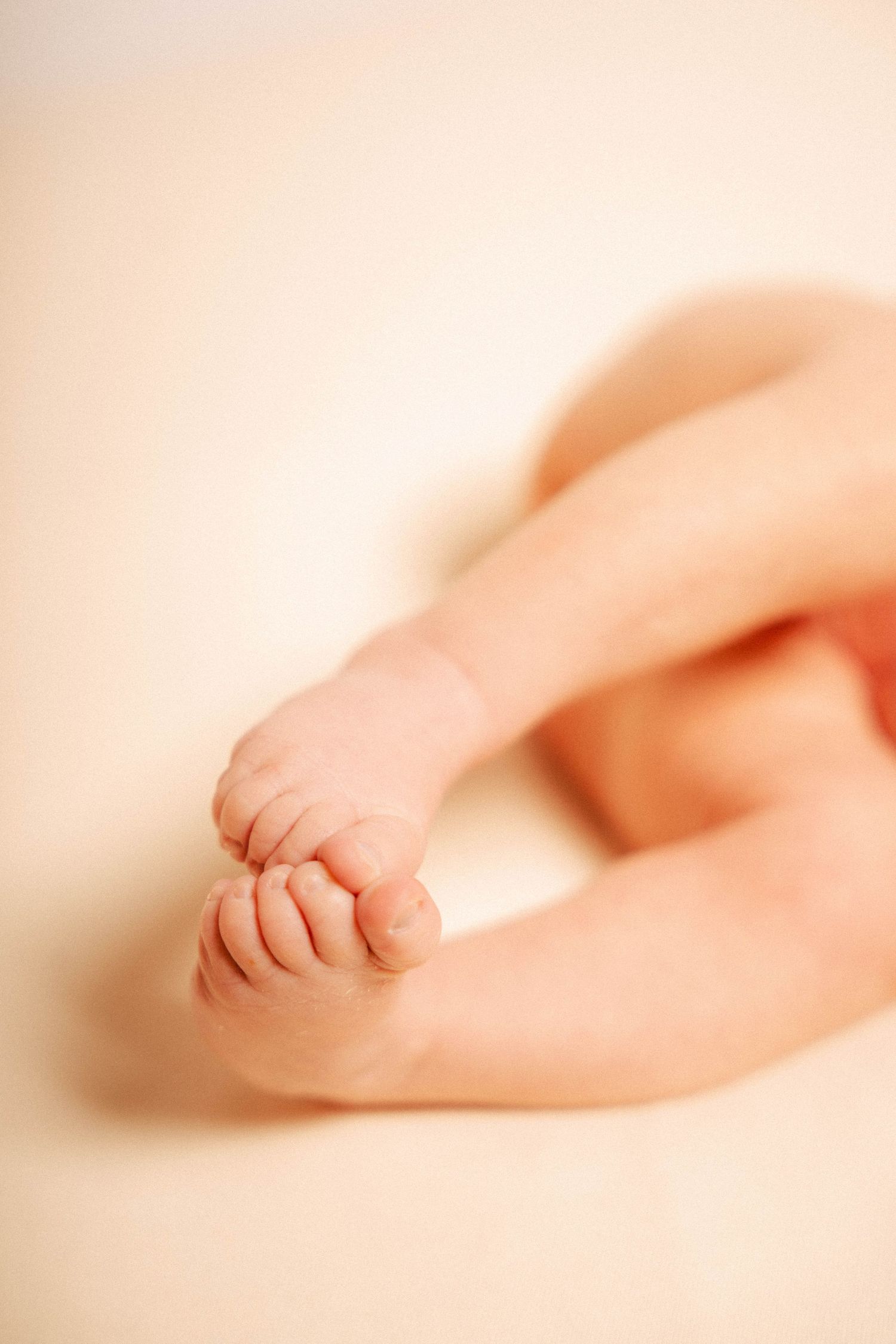 Close-up photo of tiny baby feet in soft focus against a light peachy pink background.