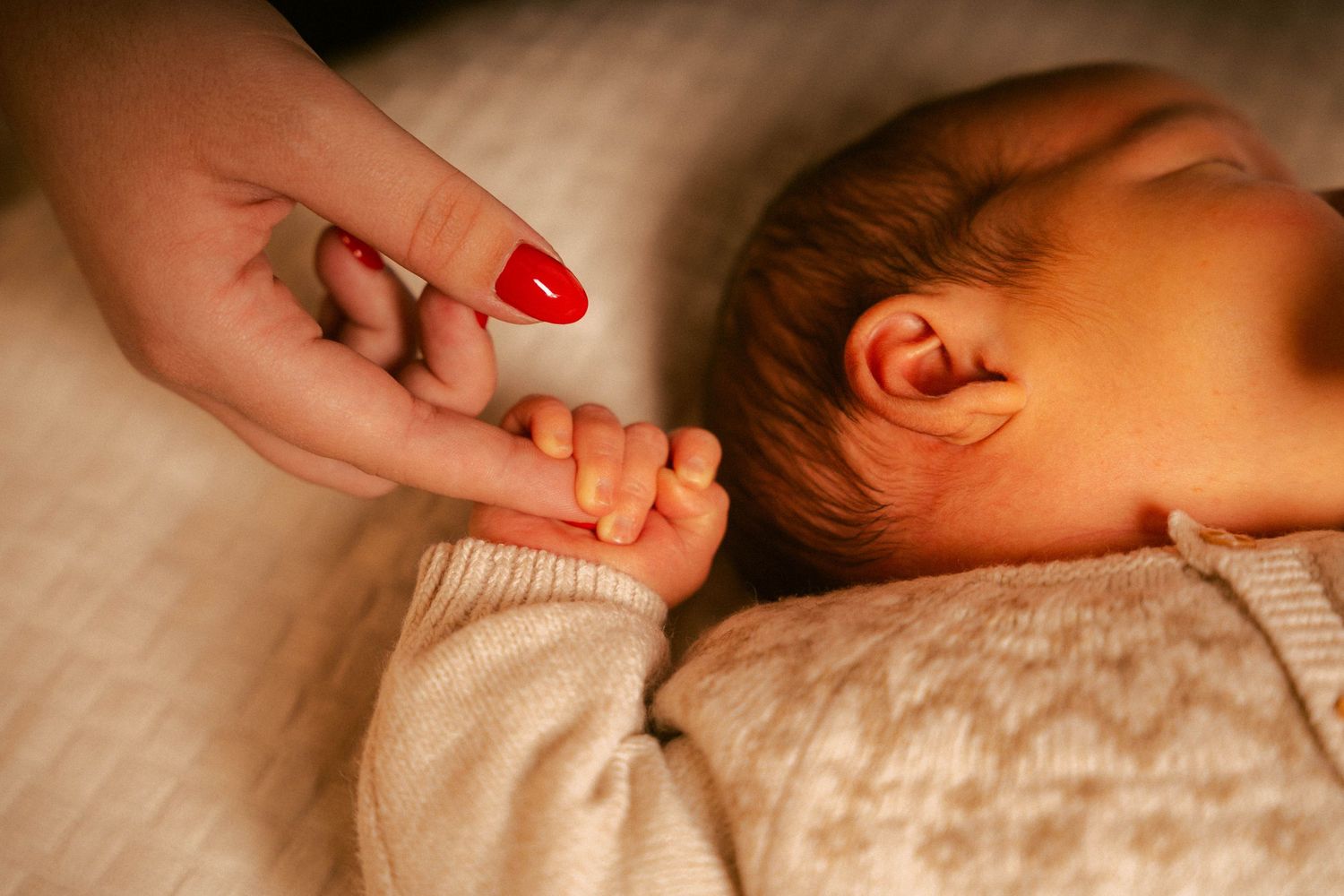 A series of hands performing a gentle baby massage on a sleeping infant lying on white bedding.