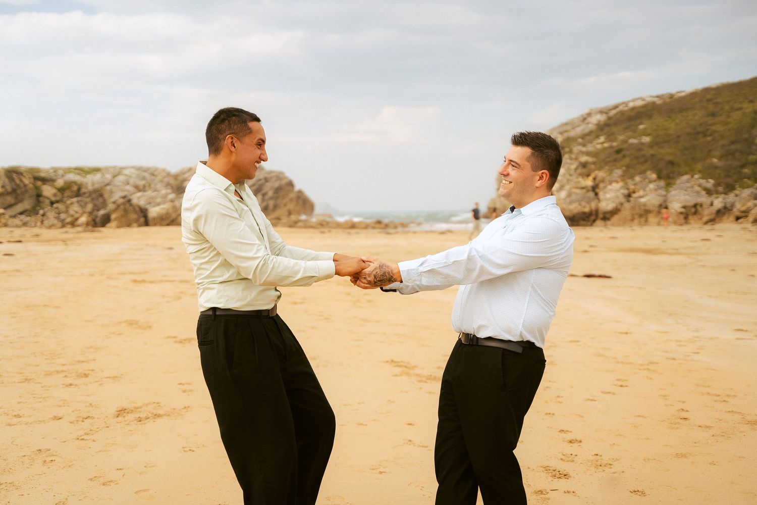 Two people in formal attire dancing playfully on a sandy beach.