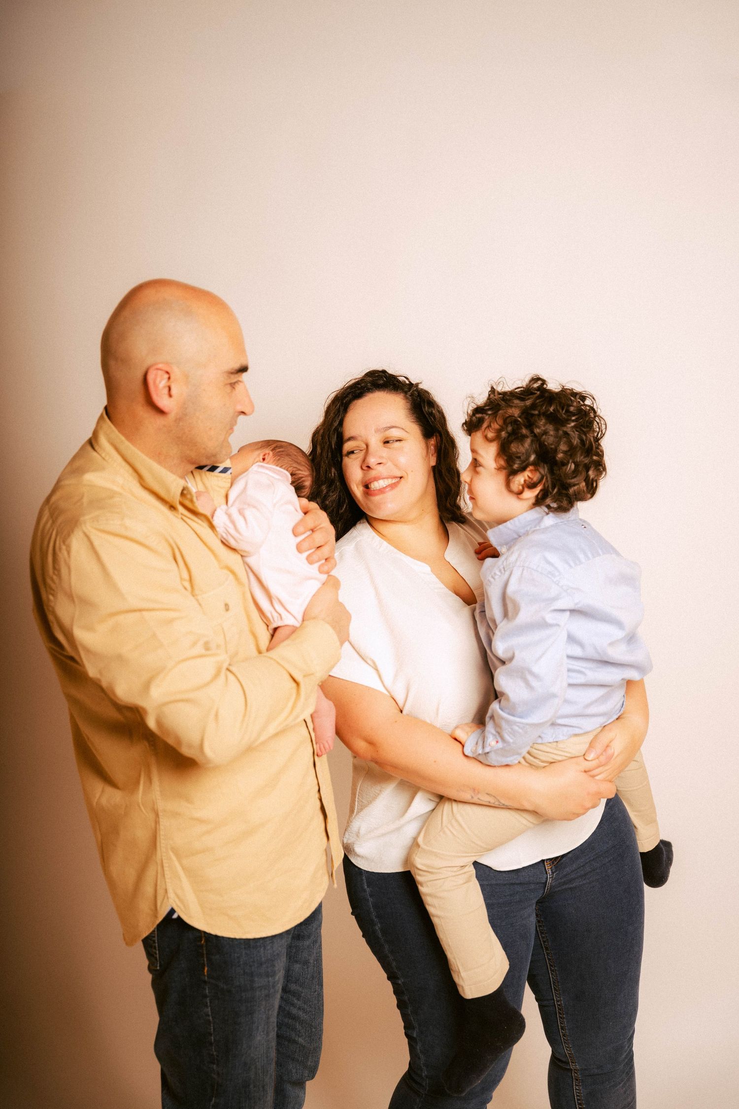 A family of three interacts playfully in a series of candid portrait shots against a neutral backdrop.