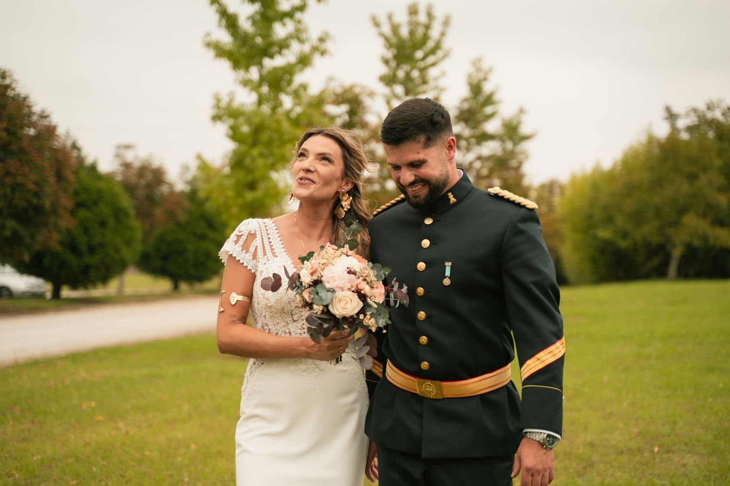 A military groom and bride share a joyful moment outdoors with autumn trees.