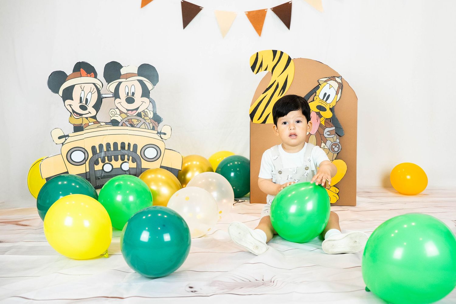 Colorful birthday party setup with Mickey Mouse decorations, balloons, and bunting against white backdrop.
