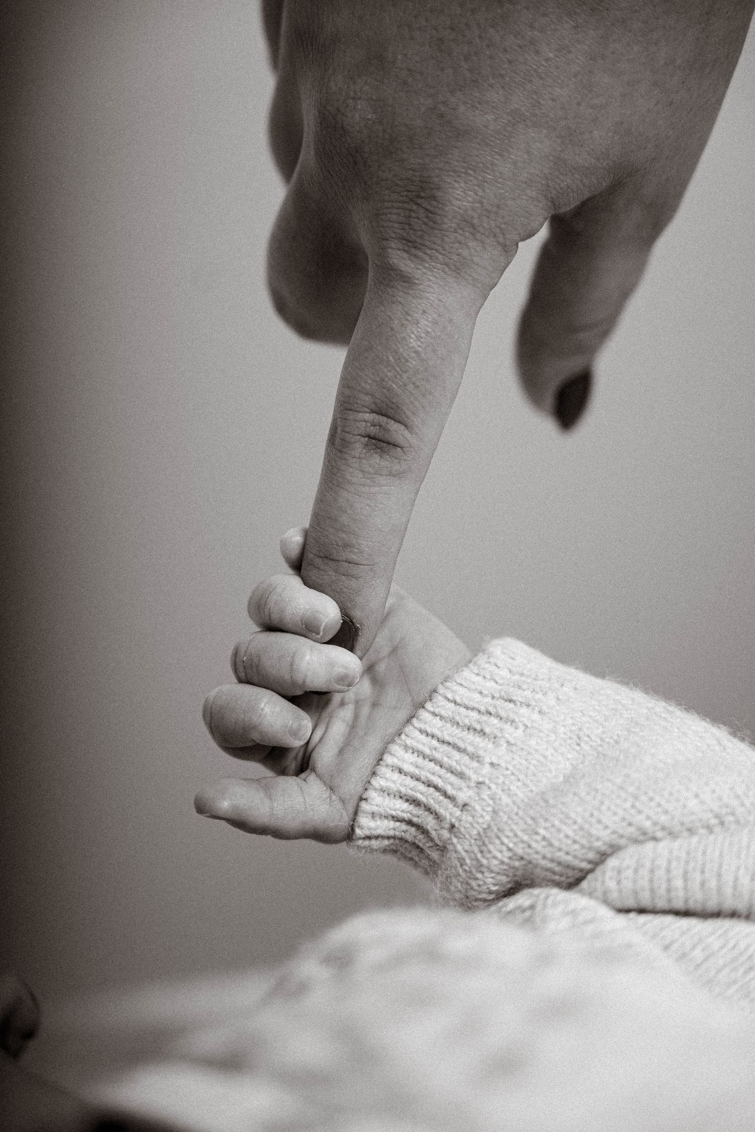 A small baby's hand grasps an adult's finger in a tender black and white photograph.
