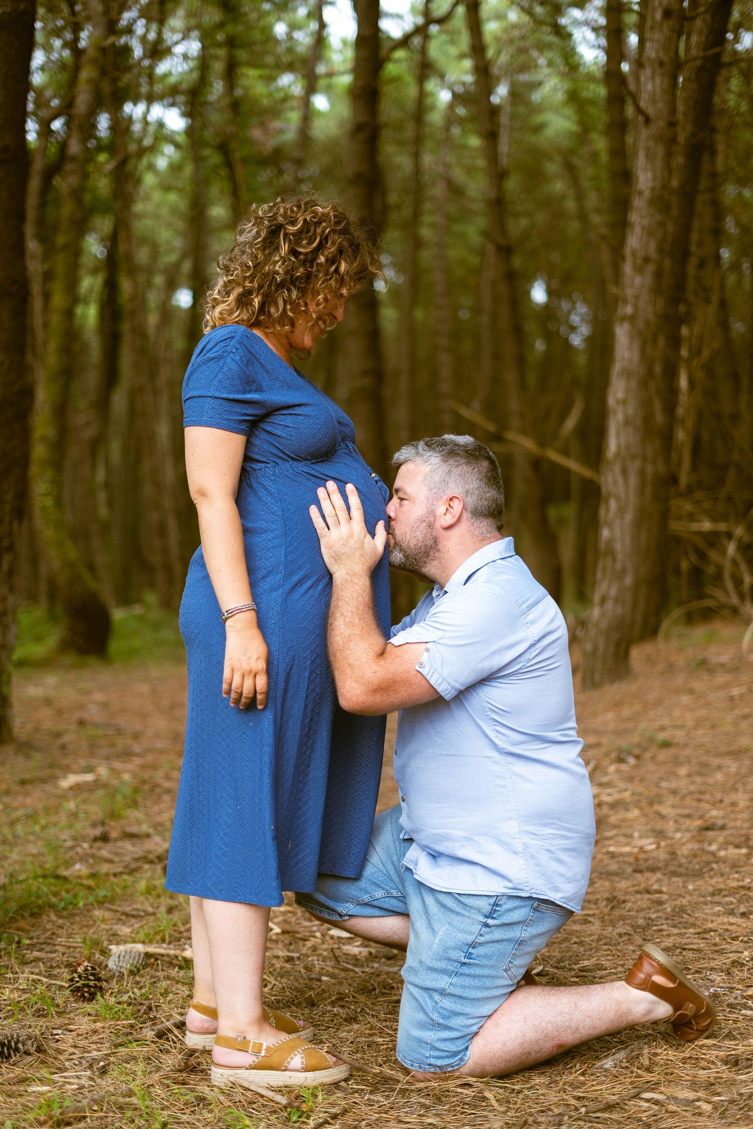 Romantic forest proposal scene with couple in blue dress and light blue shirt.