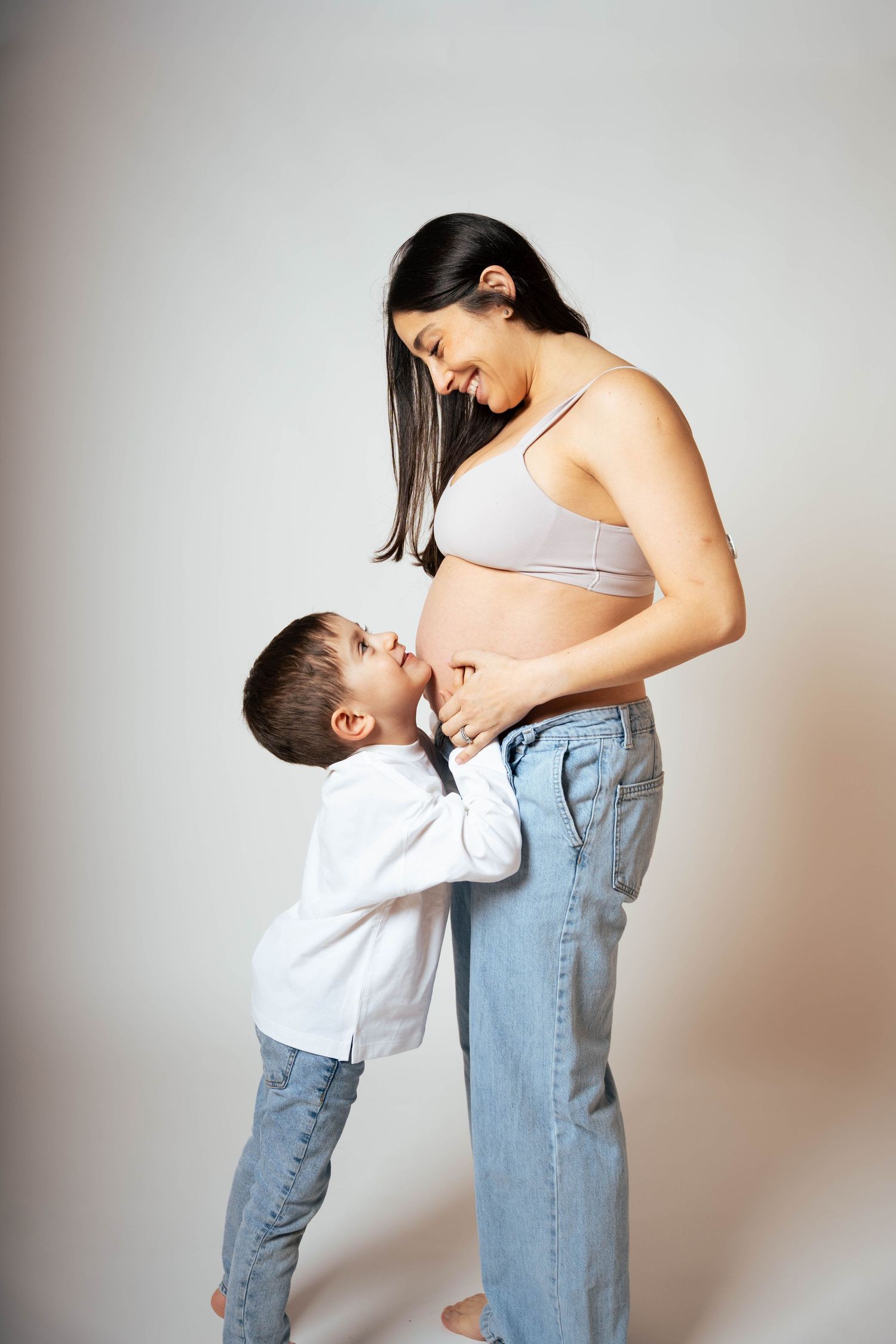 A tender moment between parent and child shows a small boy kissing a pregnant belly in a minimalist setting.