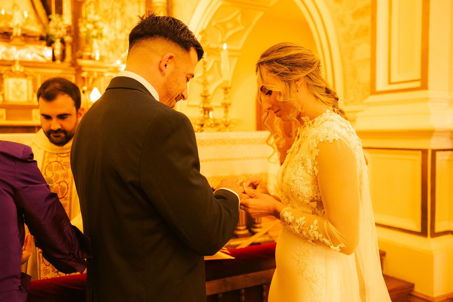 A couple exchanges rings during their wedding ceremony in a warmly lit church.