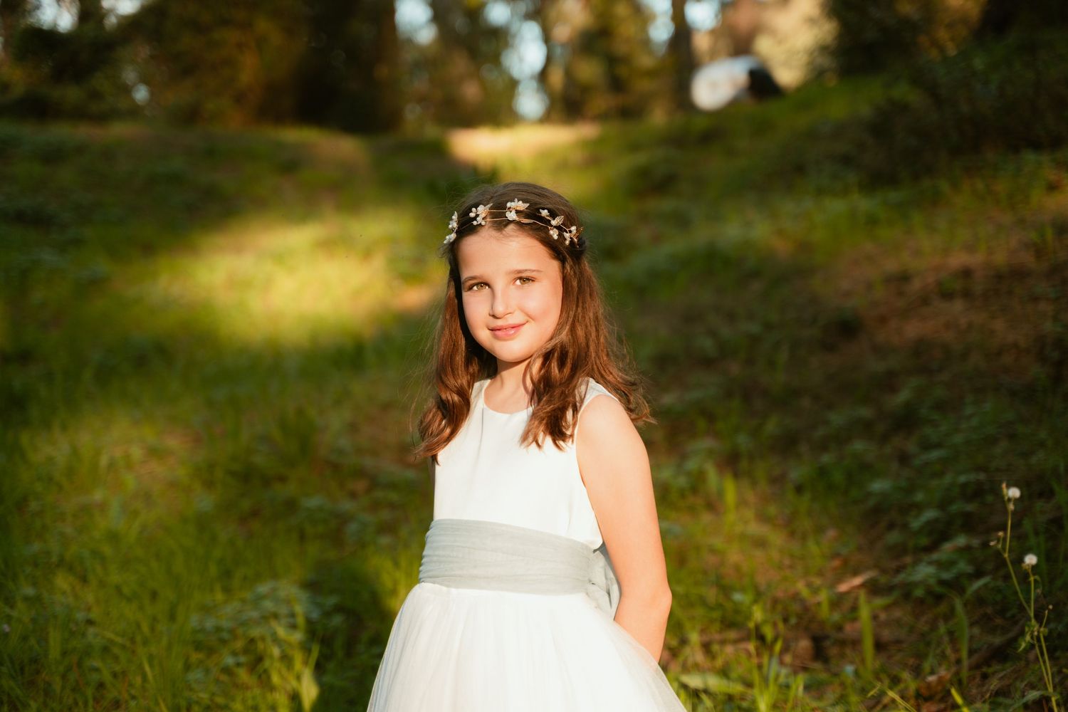 A white dress with a sage green sash photographed in a sunlit forest setting.