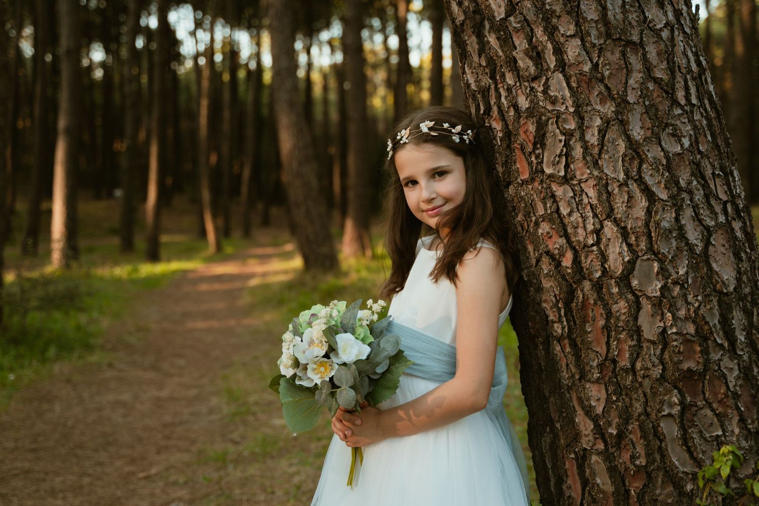 A dreamy forest portrait with a blue bouquet and white gown against a large tree trunk.