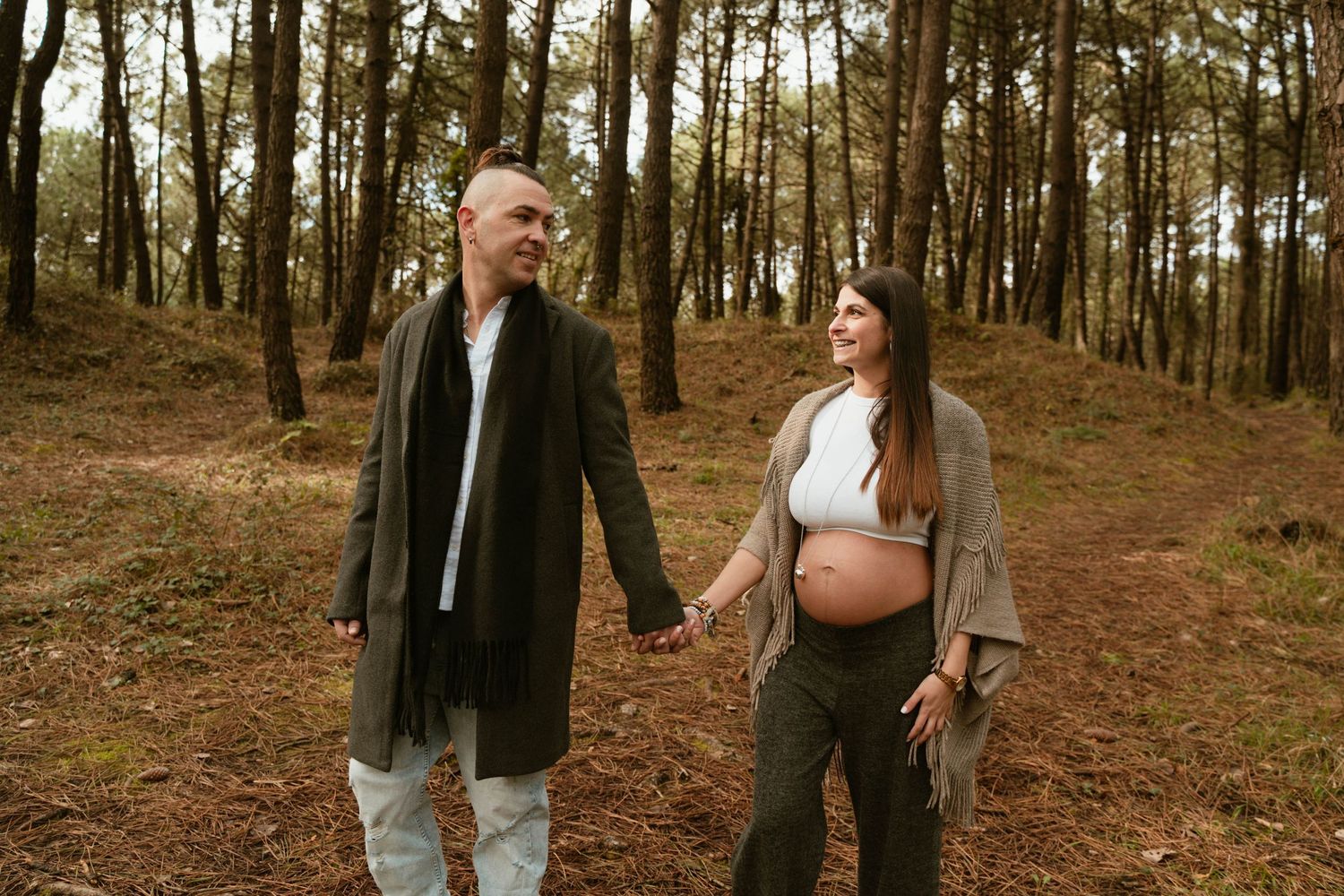 Couple walking hand in hand through a wooded forest trail during a maternity photoshoot.