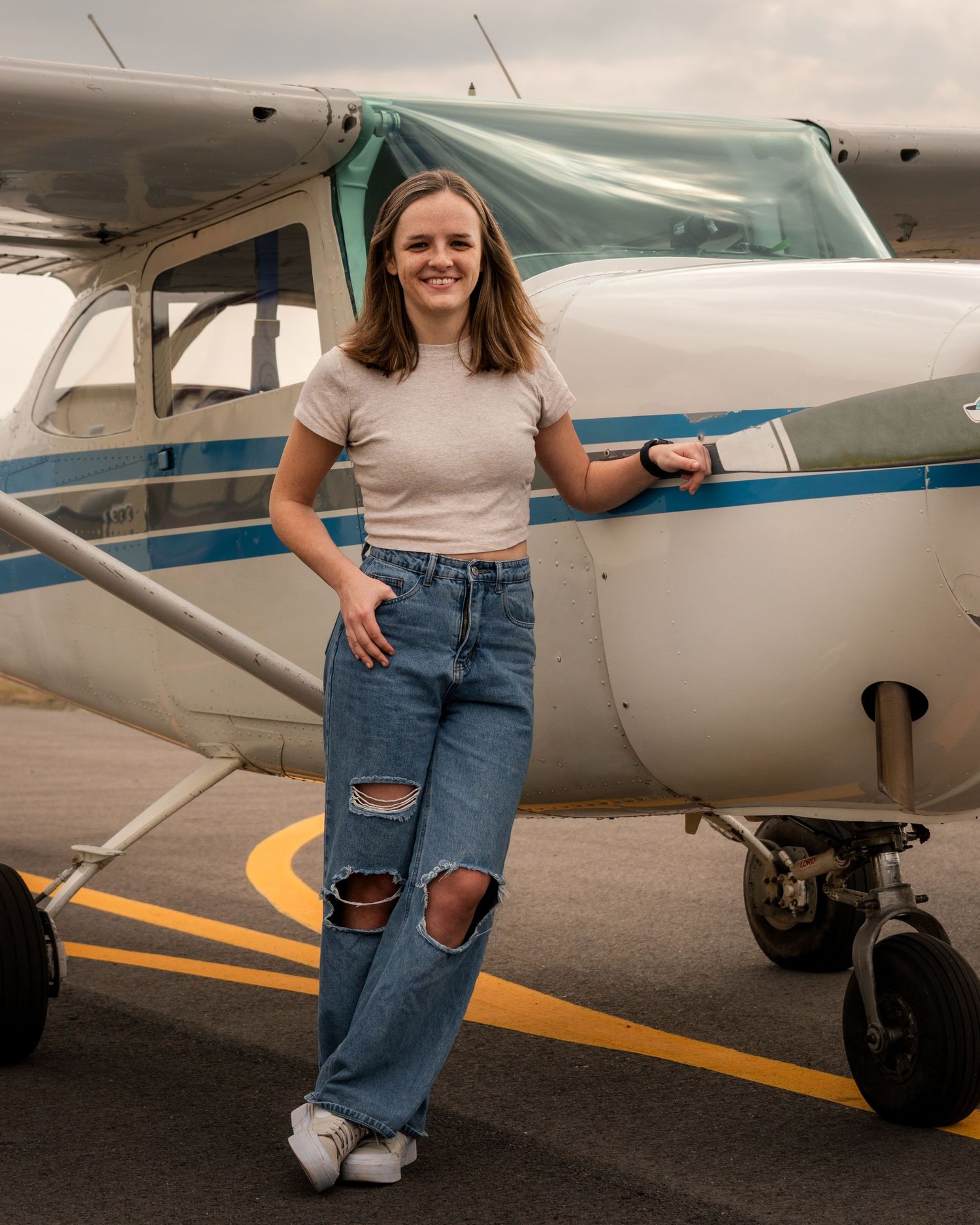 Female pilot posing beside small airplane during lifestyle portrait session at Booneville Airport in Arkansas