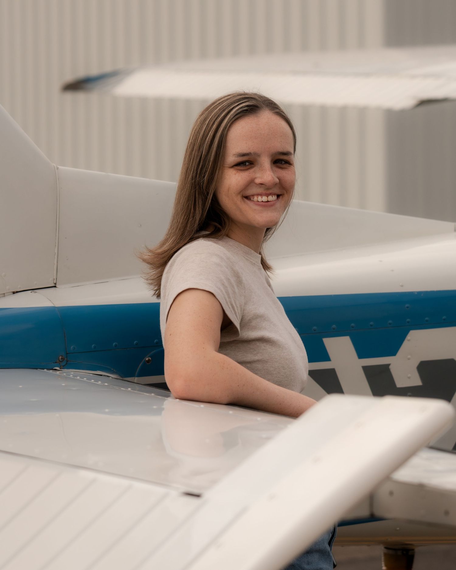 Female pilot leaning on airplane wing during lifestyle portrait session at Booneville Airport in Arkansas