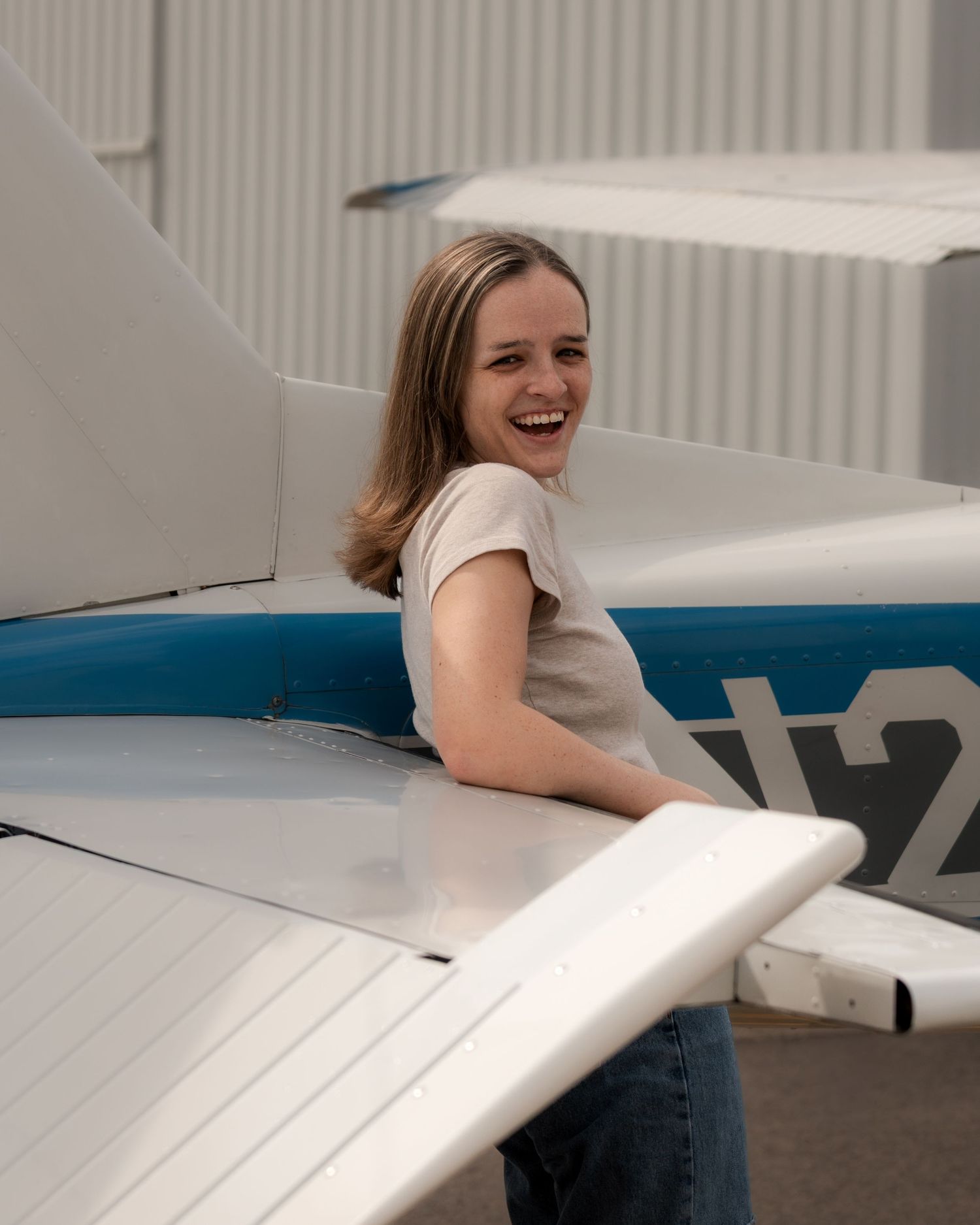 Female pilot leaning on airplane wing during lifestyle portrait session at Booneville Airport in Arkansas