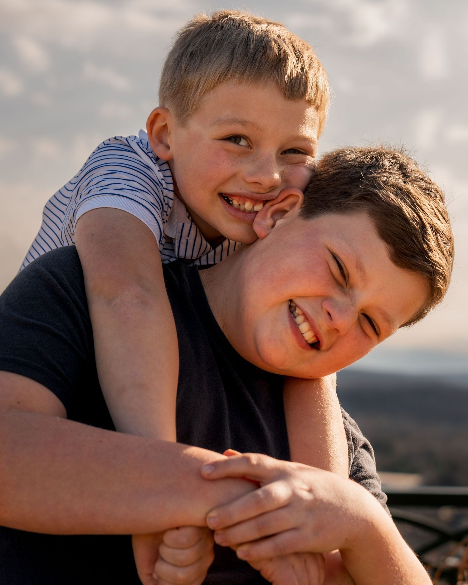Brothers laughing together with one hugging from behind during golden hour family session at Bell Park Greenwood Arkansas