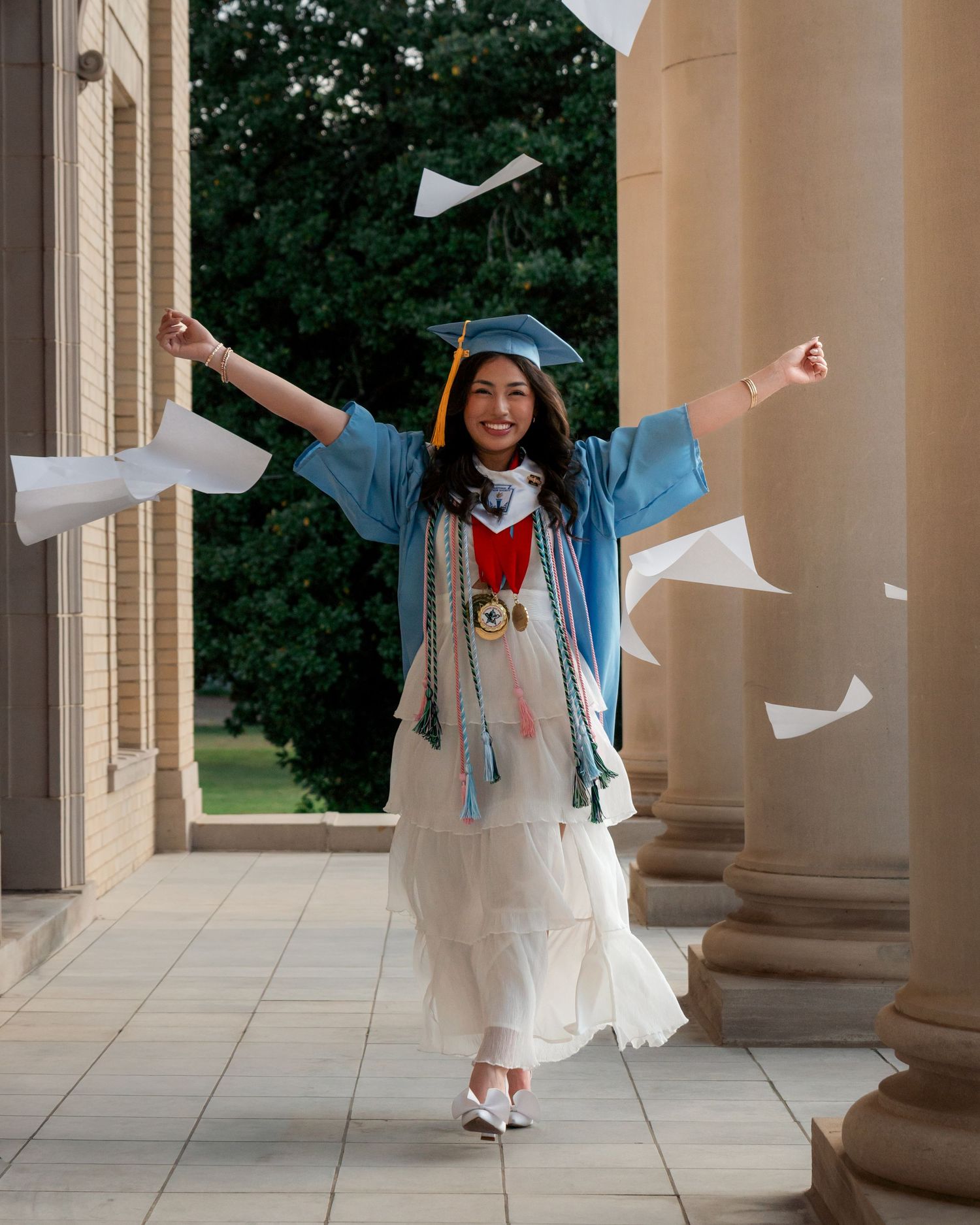 Senior graduate celebrating with arms raised as papers fly in the air during Fort Smith Arkansas photo session