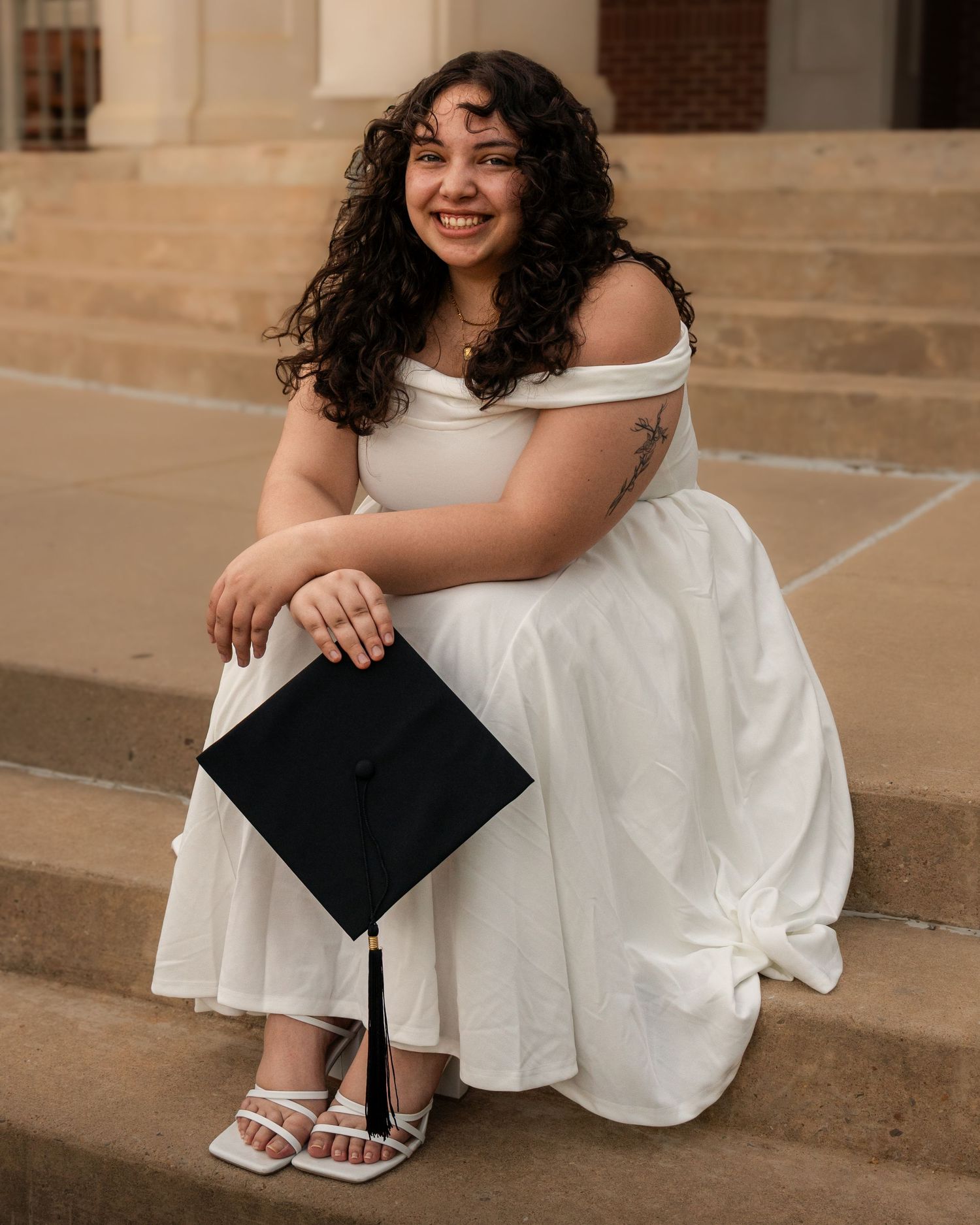 College graduate sitting on campus steps holding cap and gown during senior session at Arkansas Tech University