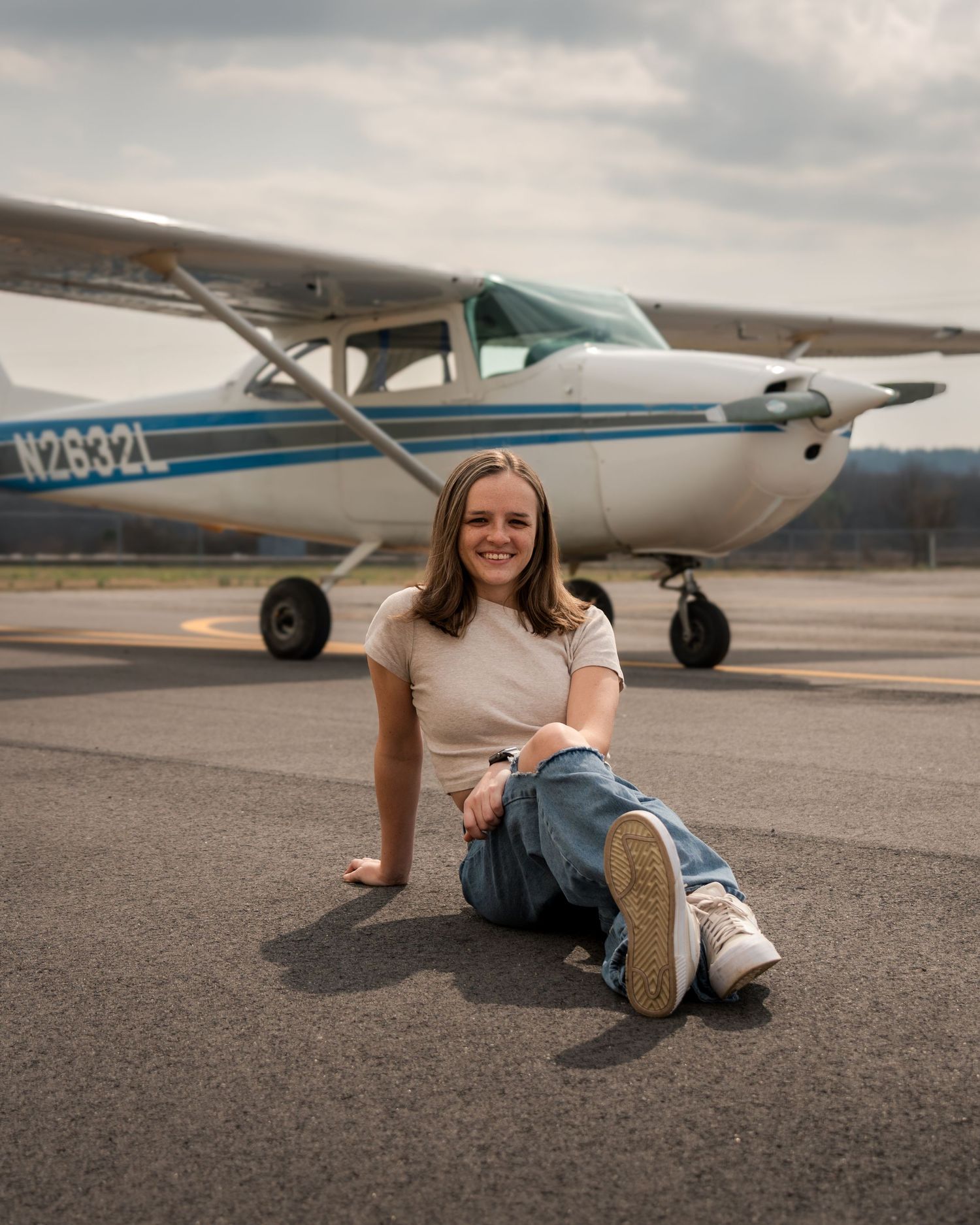 Female pilot sitting on runway in front of airplane during aviation lifestyle photoshoot at Booneville Airport Arkansas
