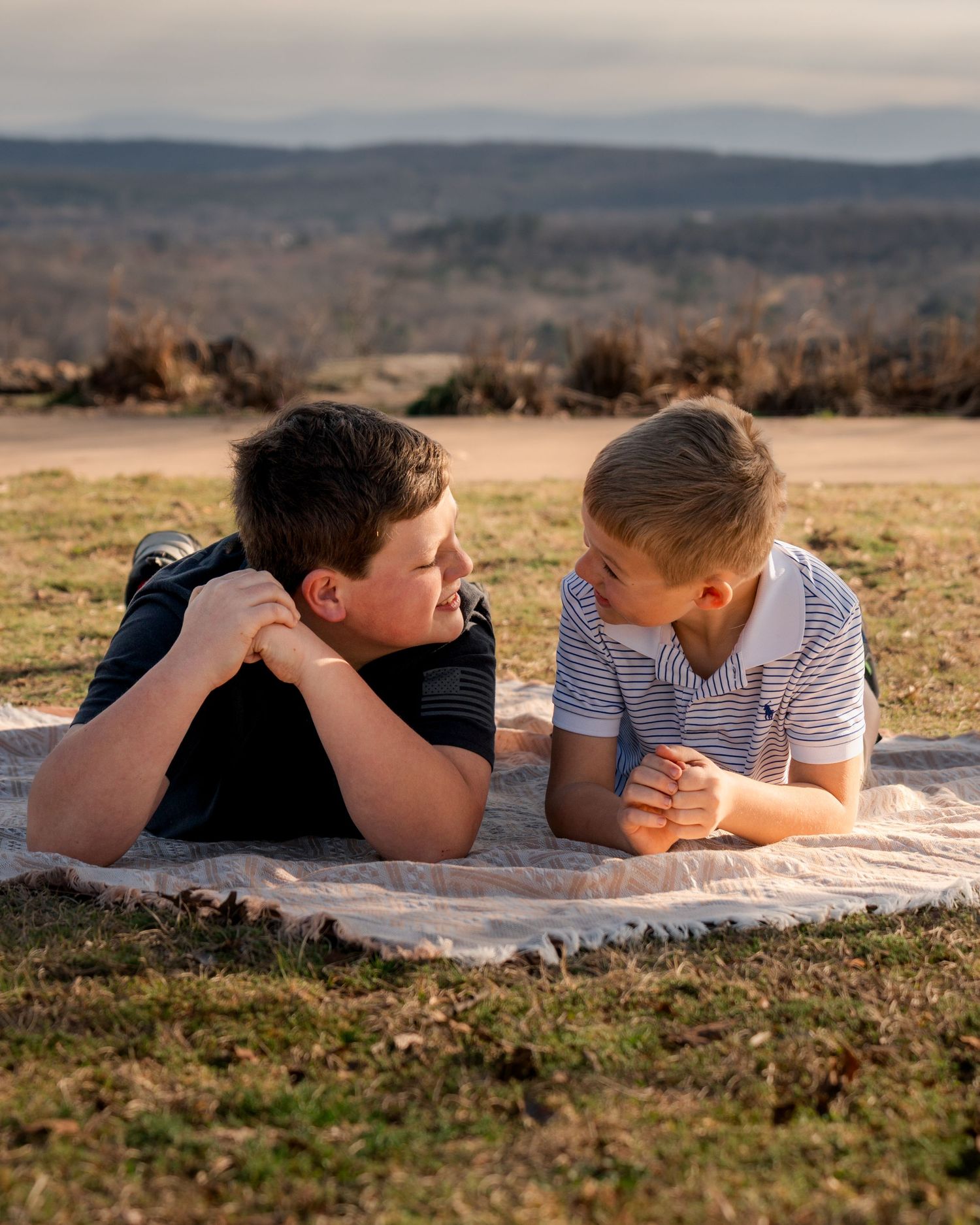 Brothers laying on blanket facing each other smiling during sunset family session at Bell Park Greenwood Arkansas