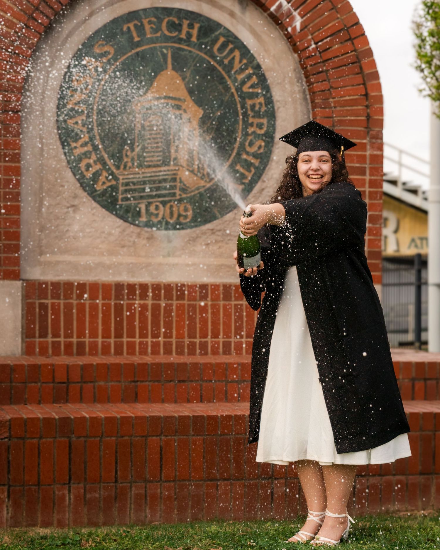 College senior graduate popping champagne in cap and gown at Arkansas Tech University campus in Russellville Arkansas