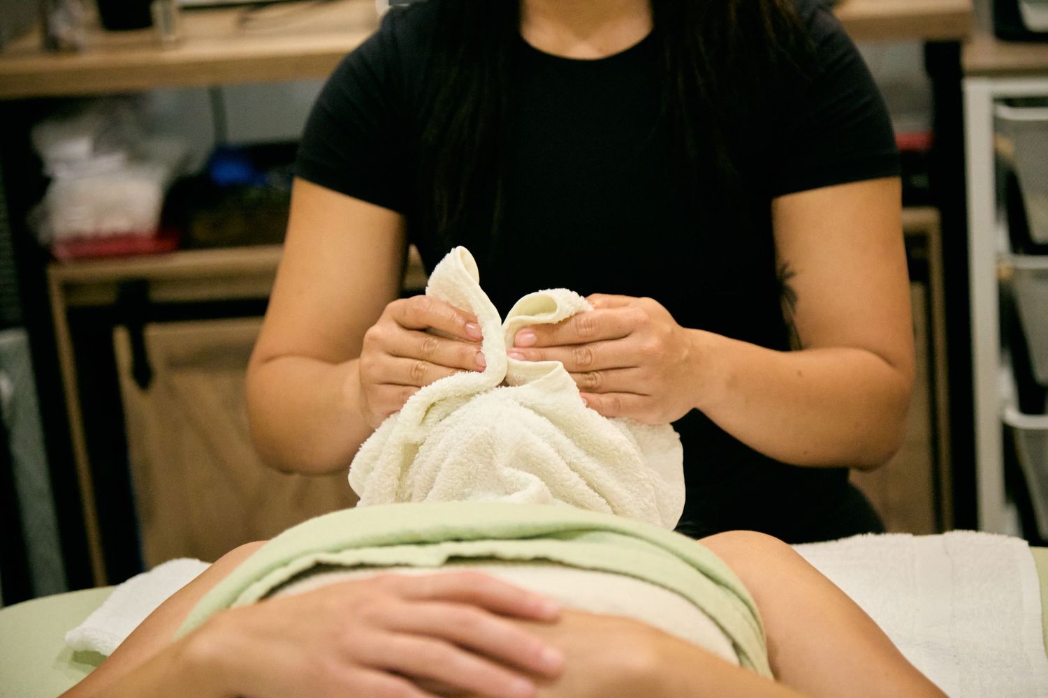 Spa therapist applying warm towel compress to client's face during relaxing facial treatment session.