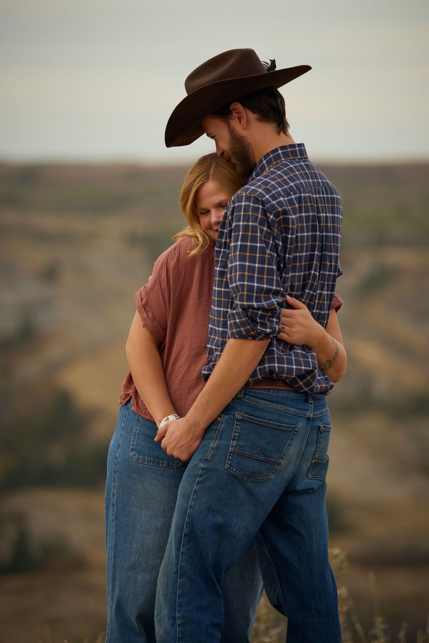 Couple in western wear embracing on a hilltop during golden hour.