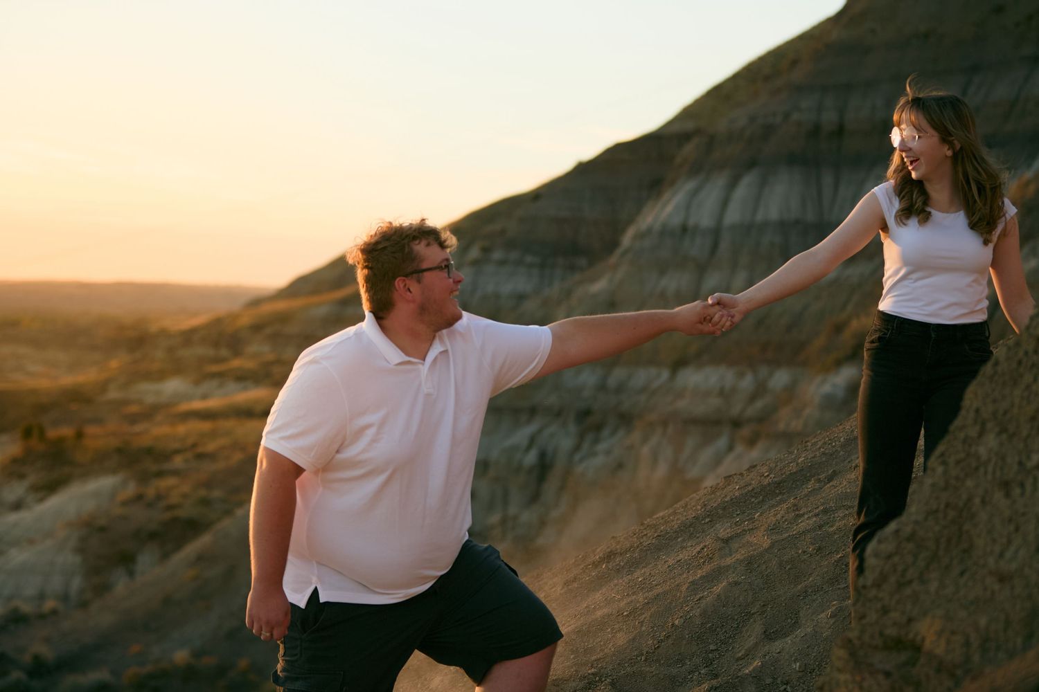 Couple holding hands against desert mountain landscape at sunset.