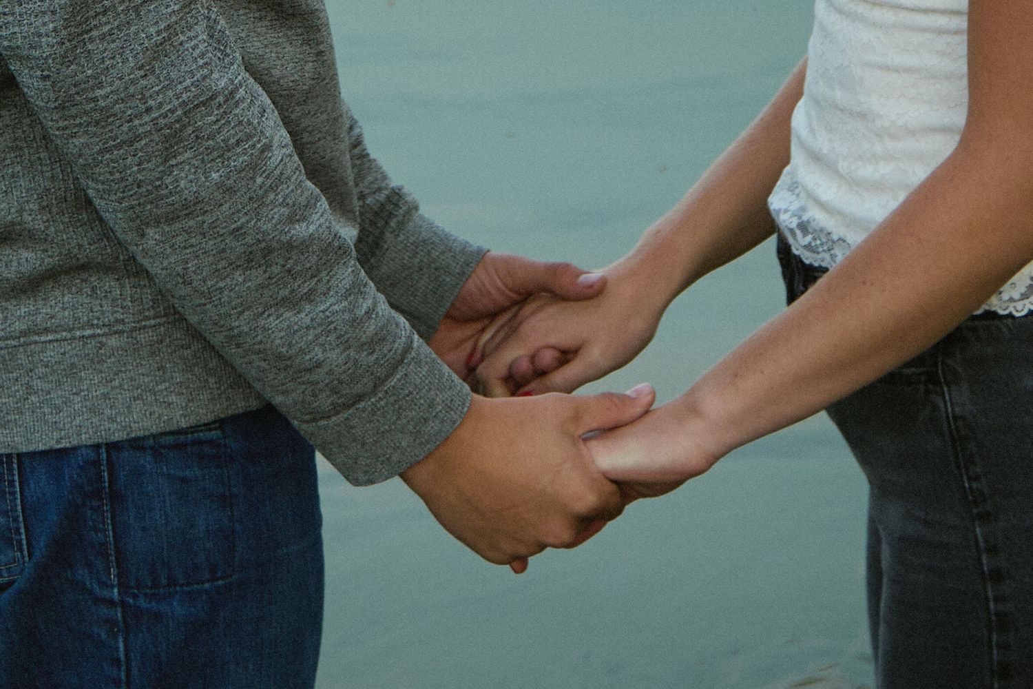 Two people holding hands tenderly outdoors, symbolizing love and connection.