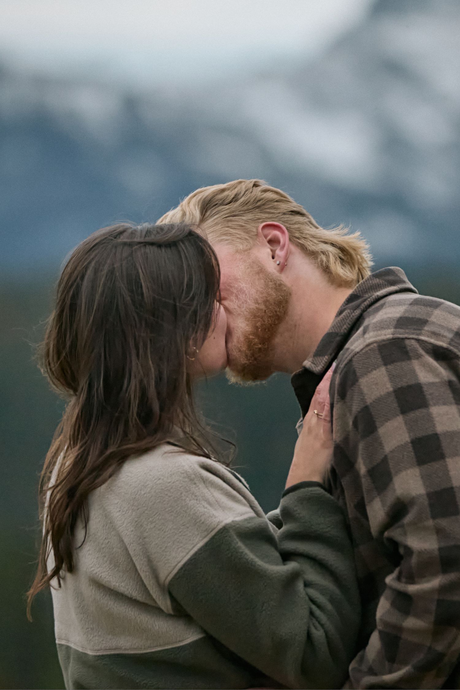 A couple shares an intimate moment while standing in front of a scenic mountain landscape.