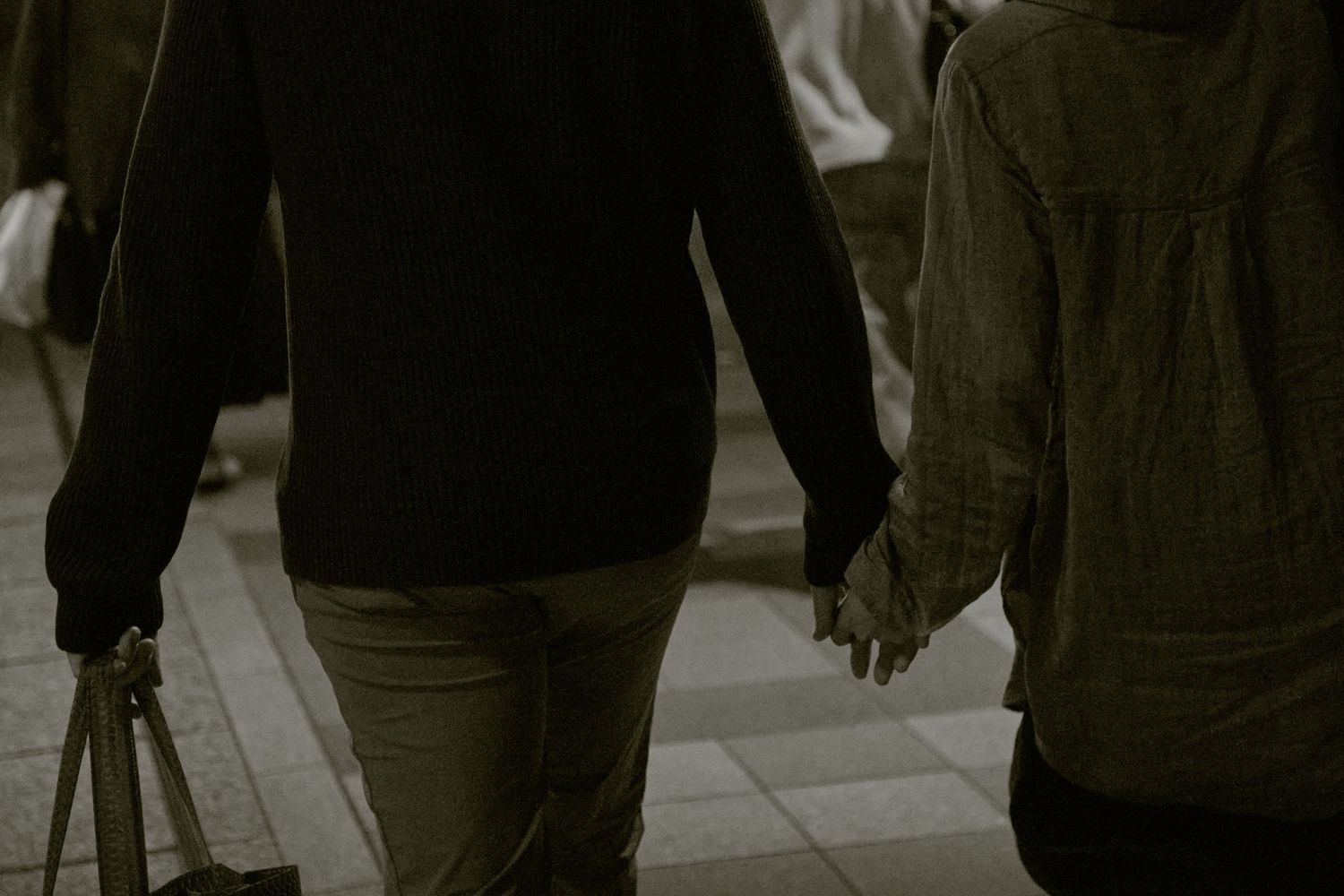 Couple holding hands while walking together on a city street, viewed from behind in a romantic moment.
