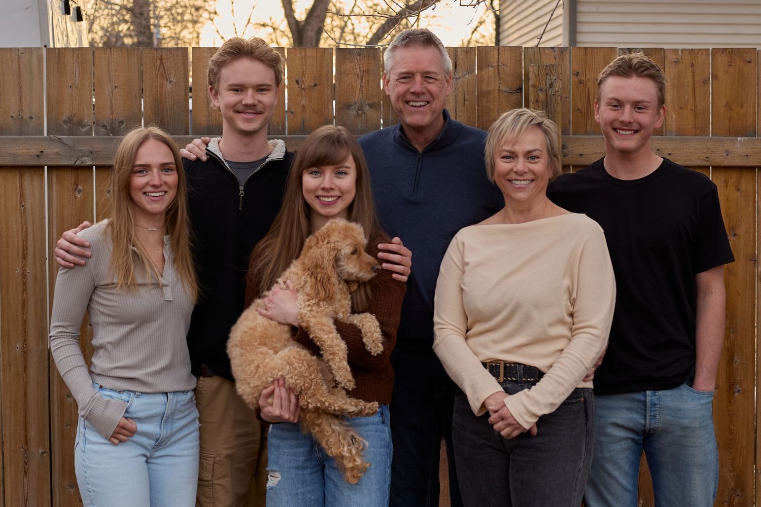 Family group poses together outdoors with a golden doodle dog.