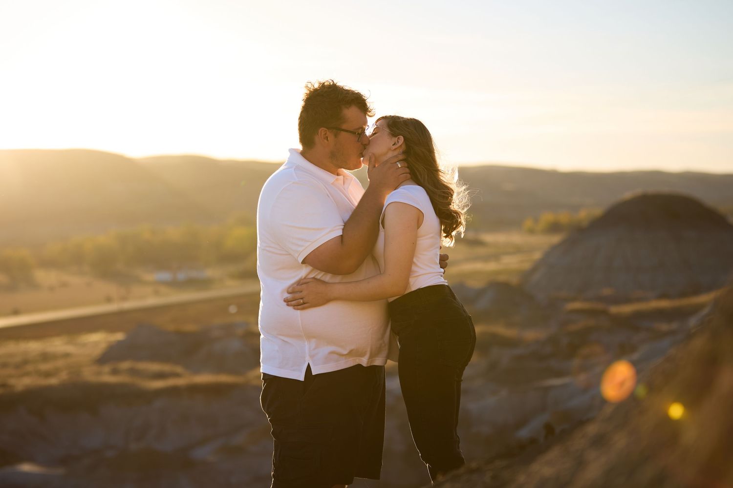 A couple embraces in silhouette against a golden sunset in a mountainous desert landscape.