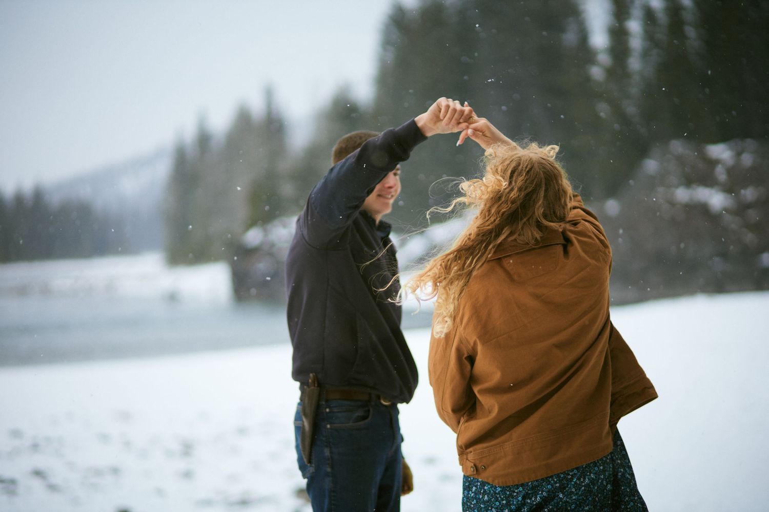 Couple dancing together in snowy winter landscape with snow-covered trees in background.