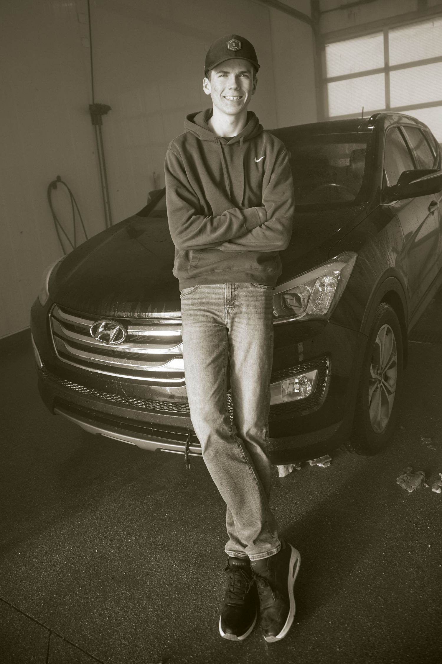 A sequence of black and white photos showing someone sitting on the hood of a dark-colored car in a garage.