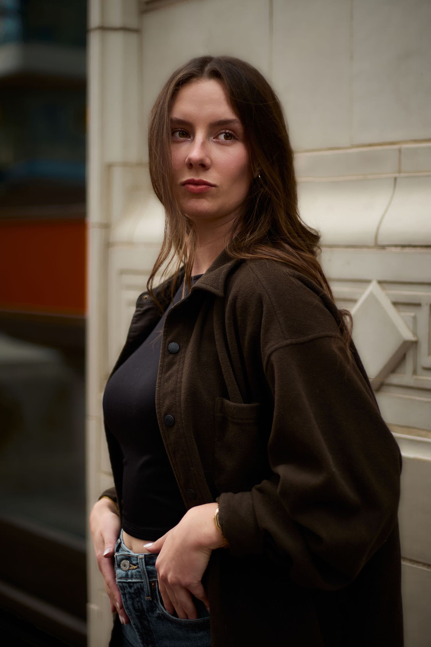 Moody urban portraits against a white wall featuring a dark jacket and casual styling.
