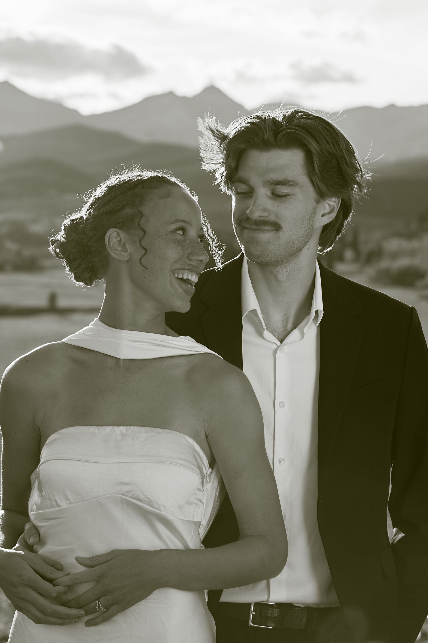 A romantic black and white photo series showing a couple embracing and sharing intimate moments against a mountain backdrop.