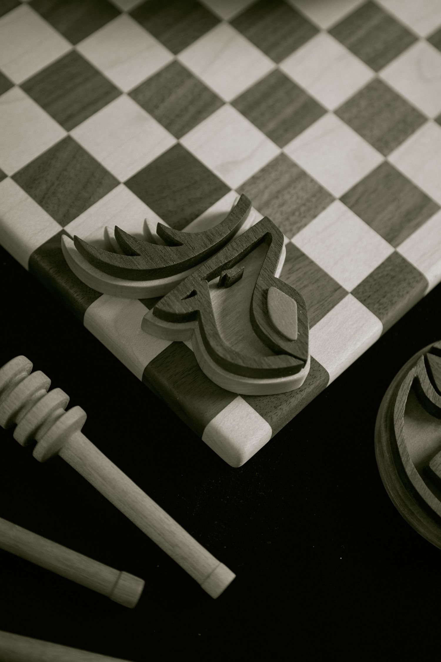 Handcrafted wooden chess pieces and board in sepia tone, featuring an artistic horse knight carving on checkered surface.