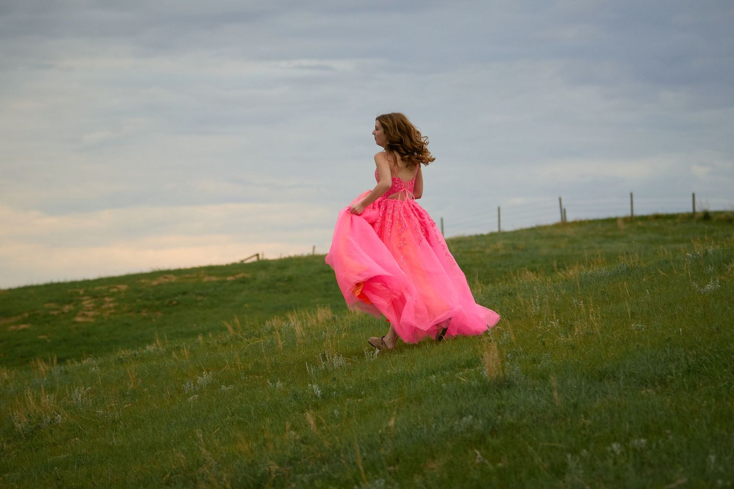 A girl in a flowing pink gown runs through a lush green field under a cloudy sky.